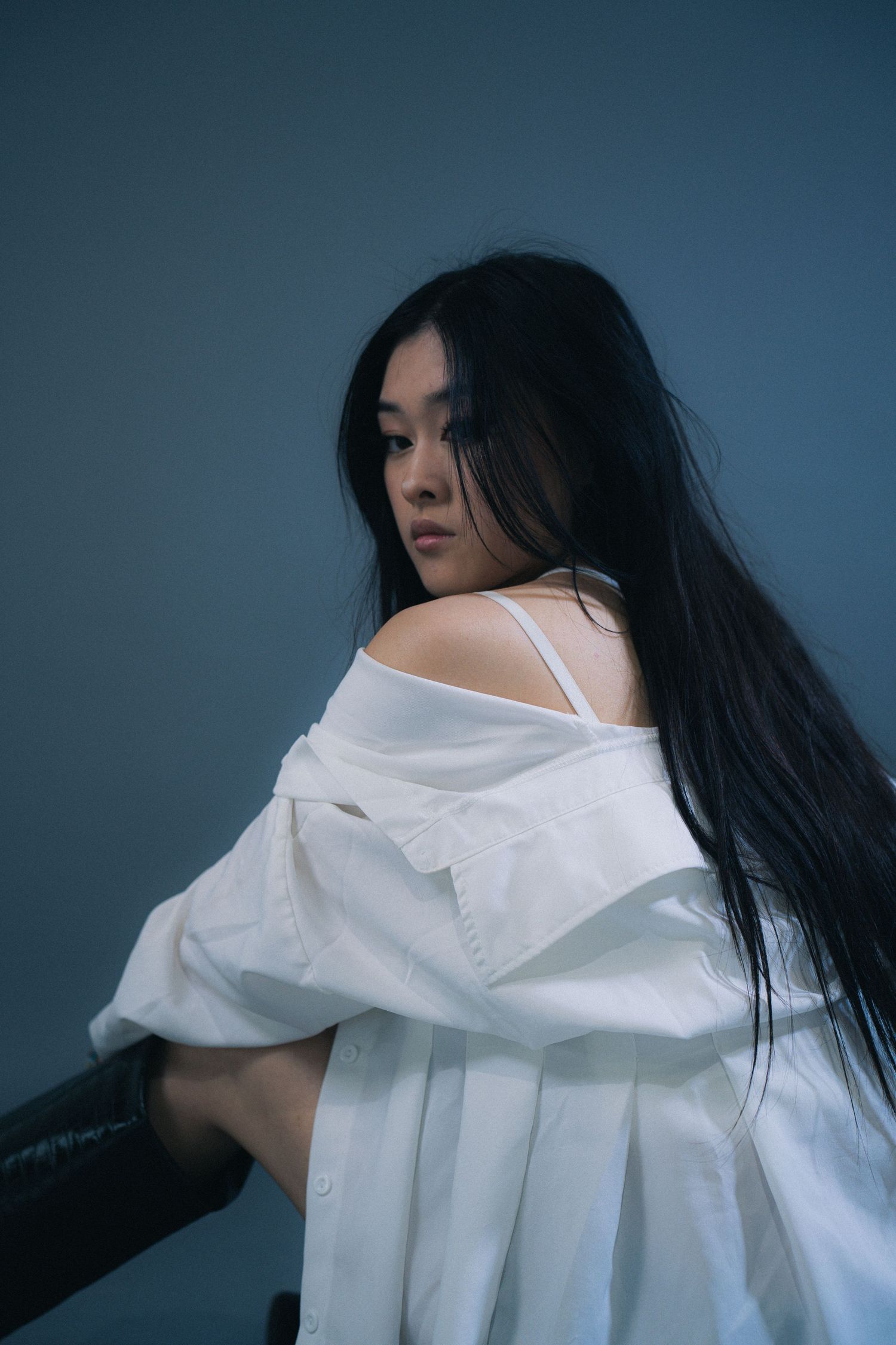 A series of artistic portraits showing a person with long dark hair in a flowing white shirt against a moody blue backdrop.