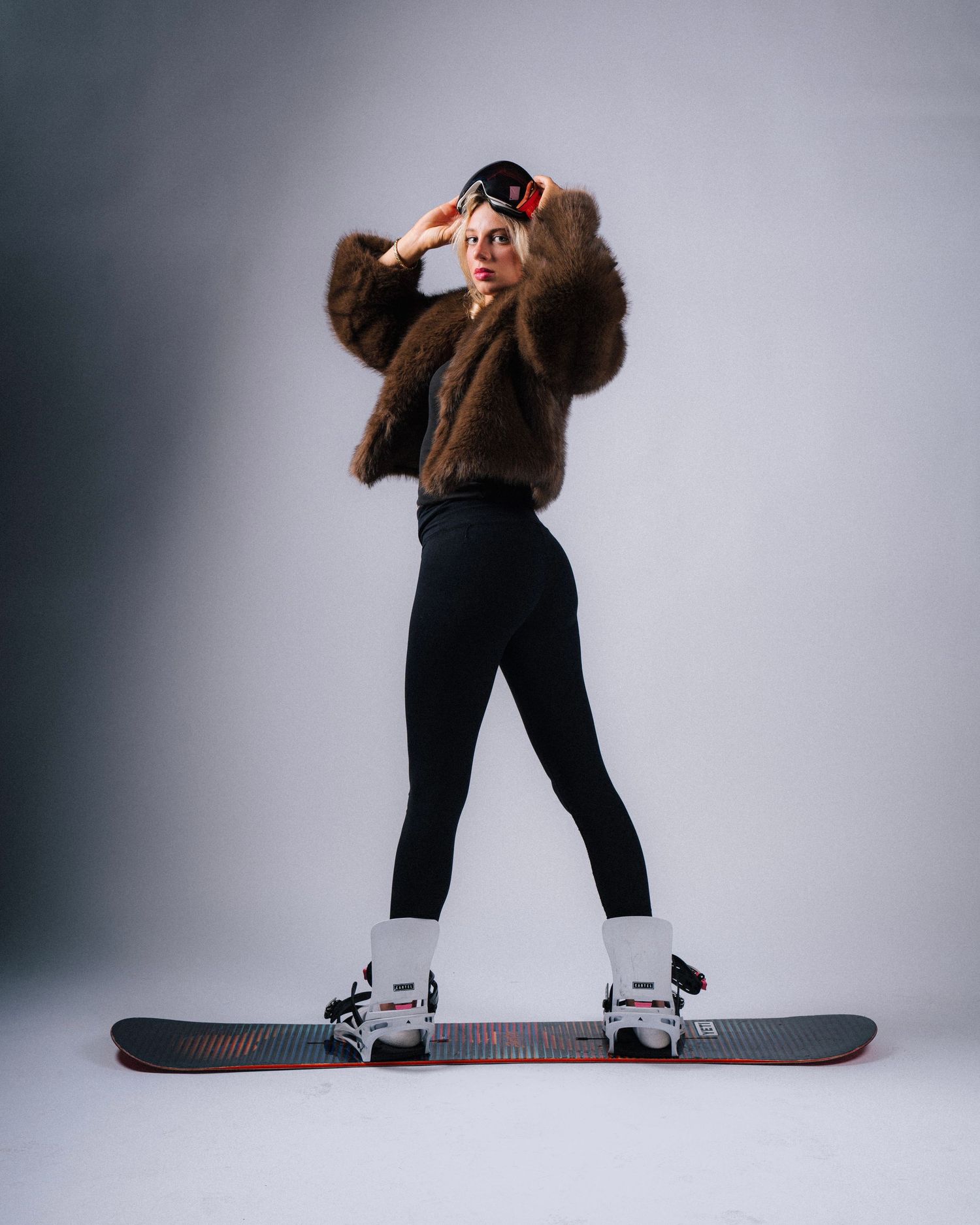 Person in brown sweater and black pants performs progressive dance movements against studio background with snowboard.