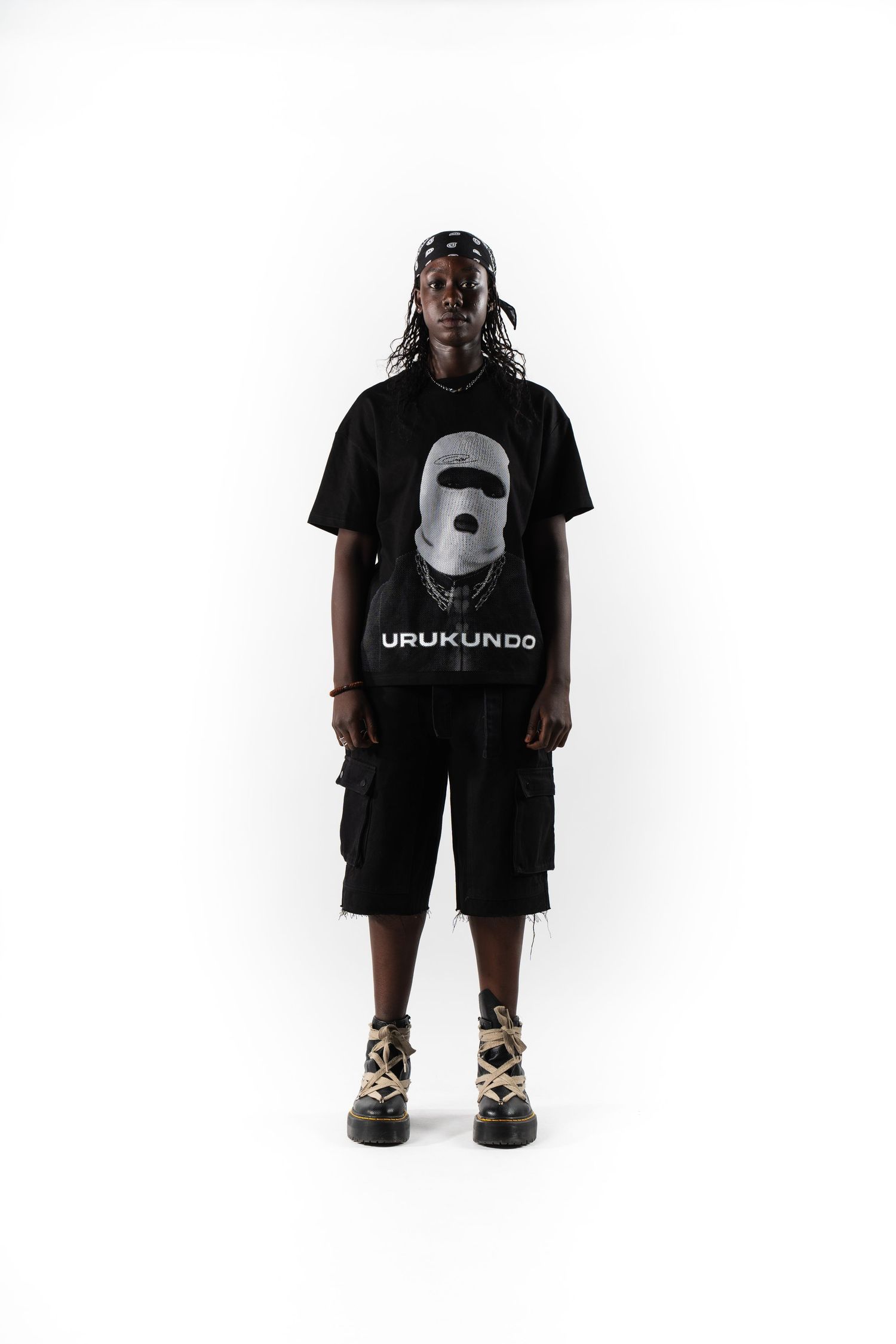 Person wearing black graphic t-shirt with cargo shorts in minimalist studio setting.