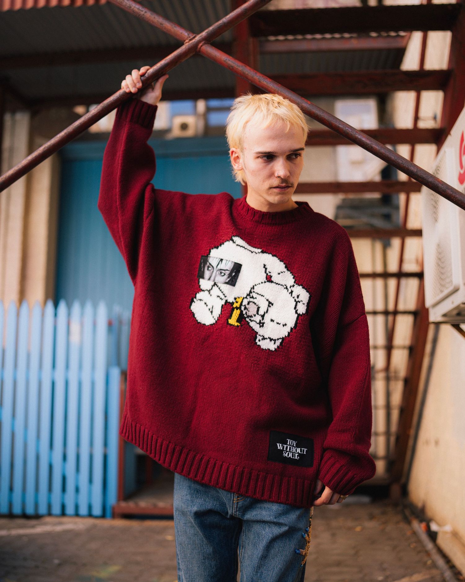 Person wearing burgundy sweater with graphic print posing against urban background.