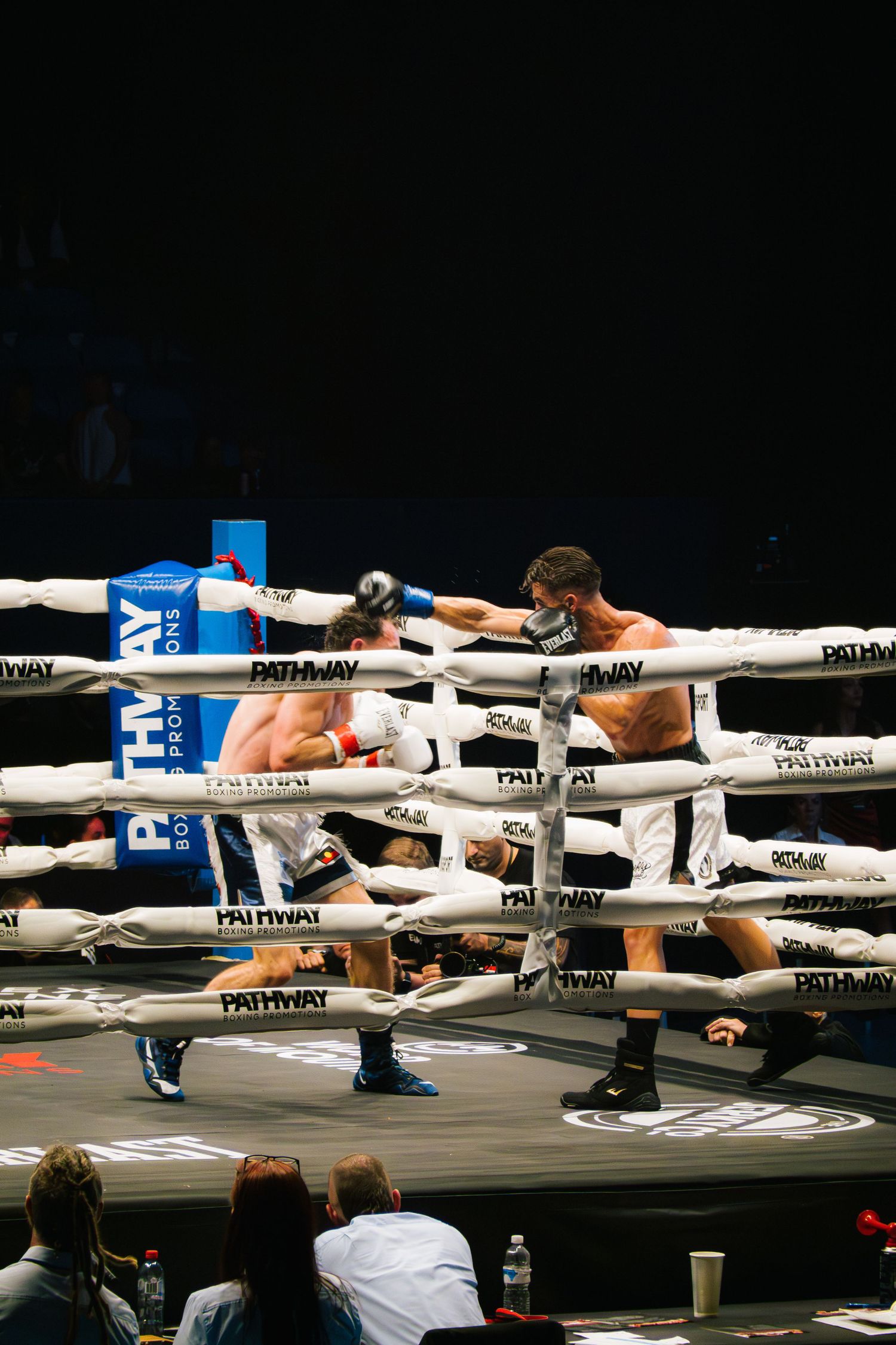 Two boxers compete in a match through the ropes of a white boxing ring.
