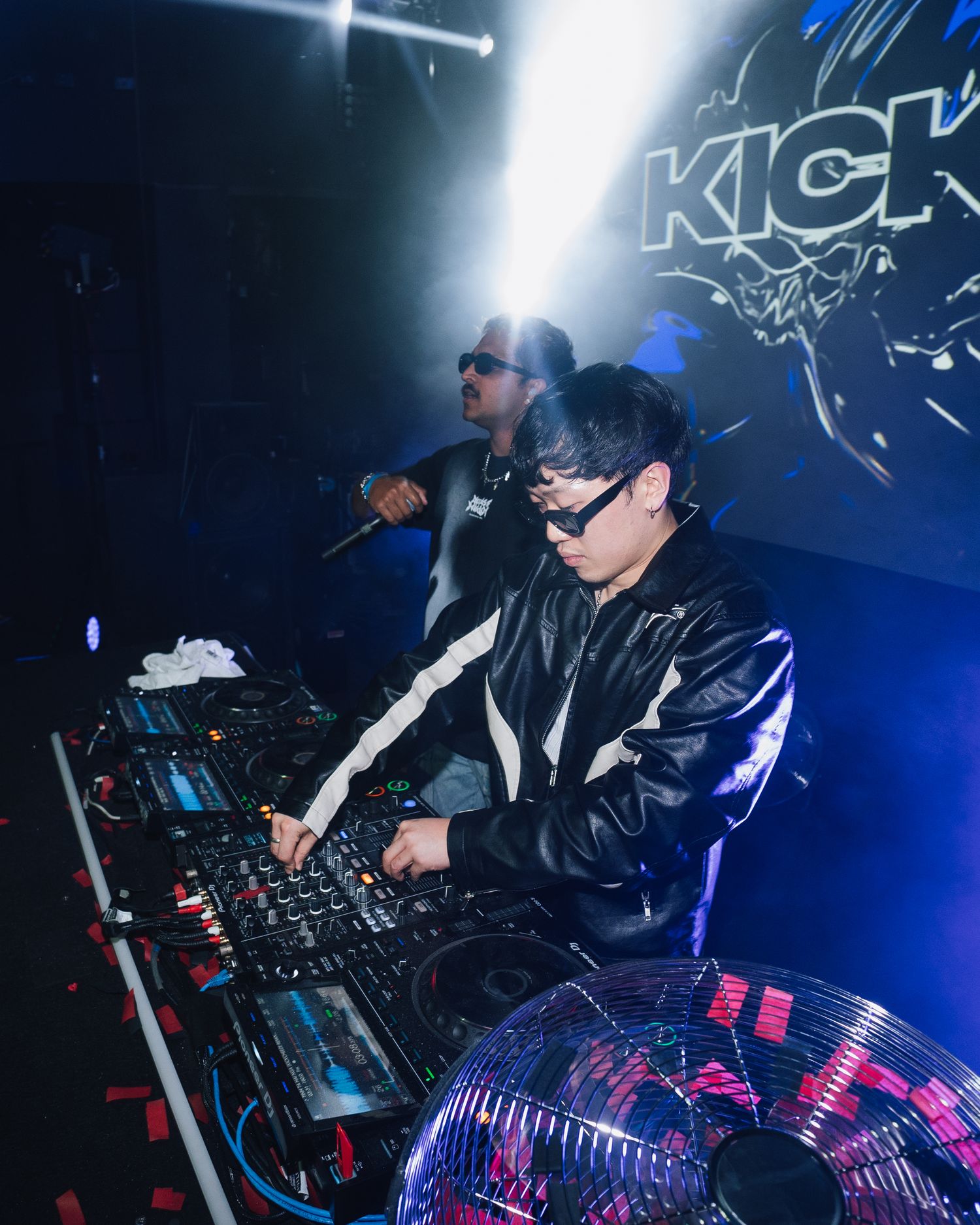DJ performing at KICK event with dramatic stage lighting and equipment setup.