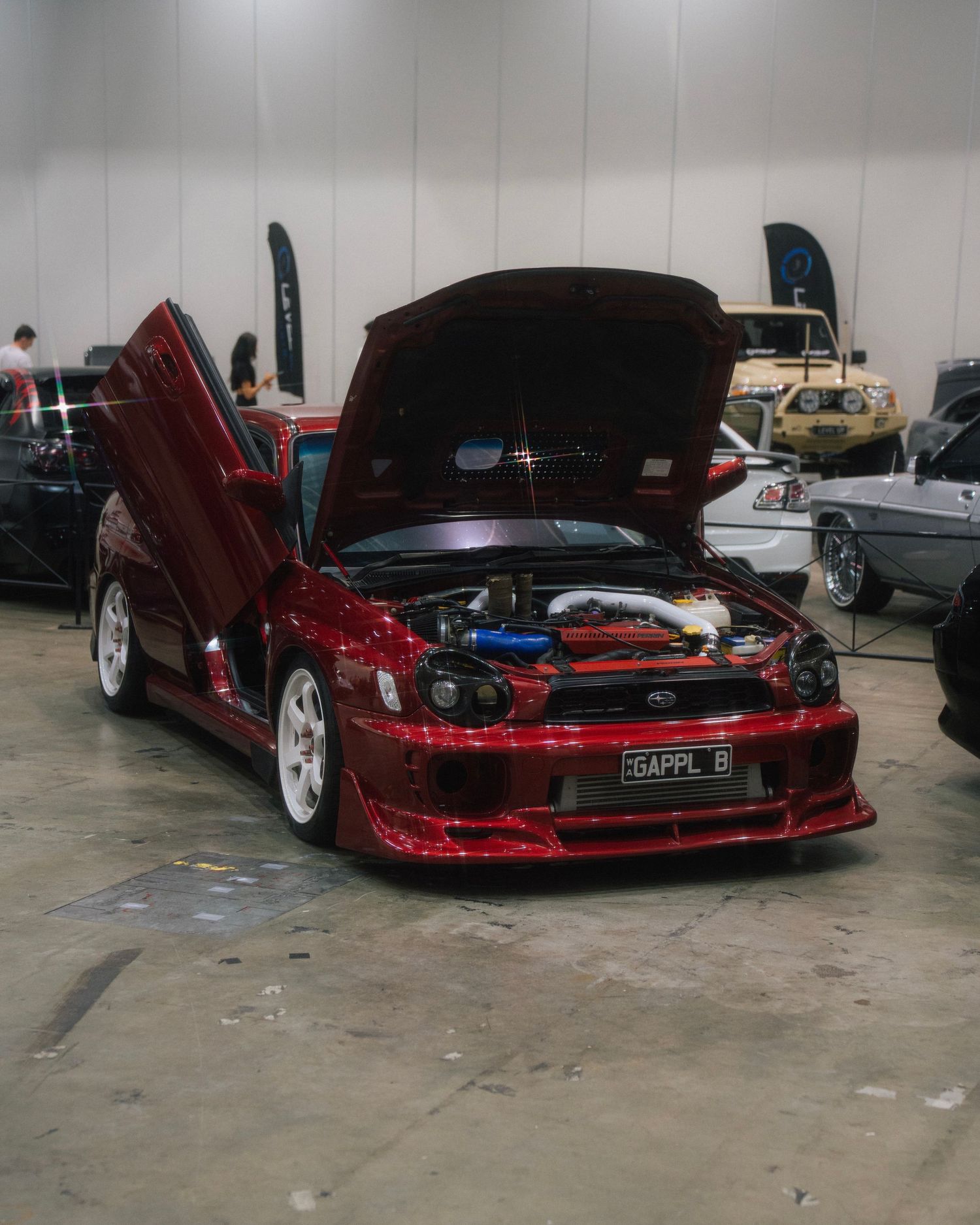 Modified red sports car with scissor doors open displaying custom engine bay modifications.
