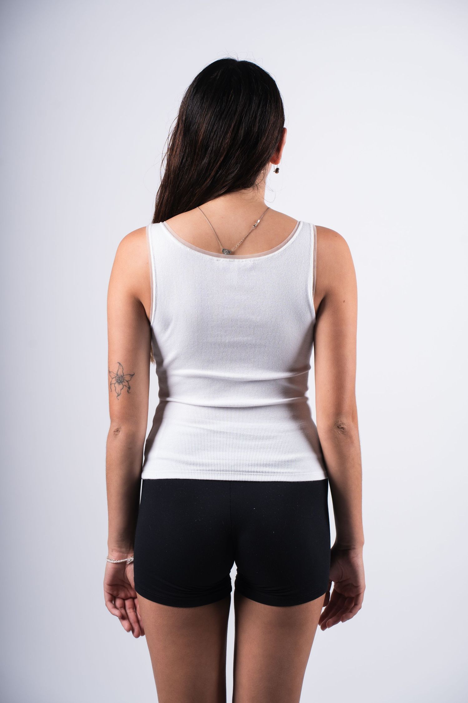 Back view of person wearing white tank top and black shorts against neutral background.