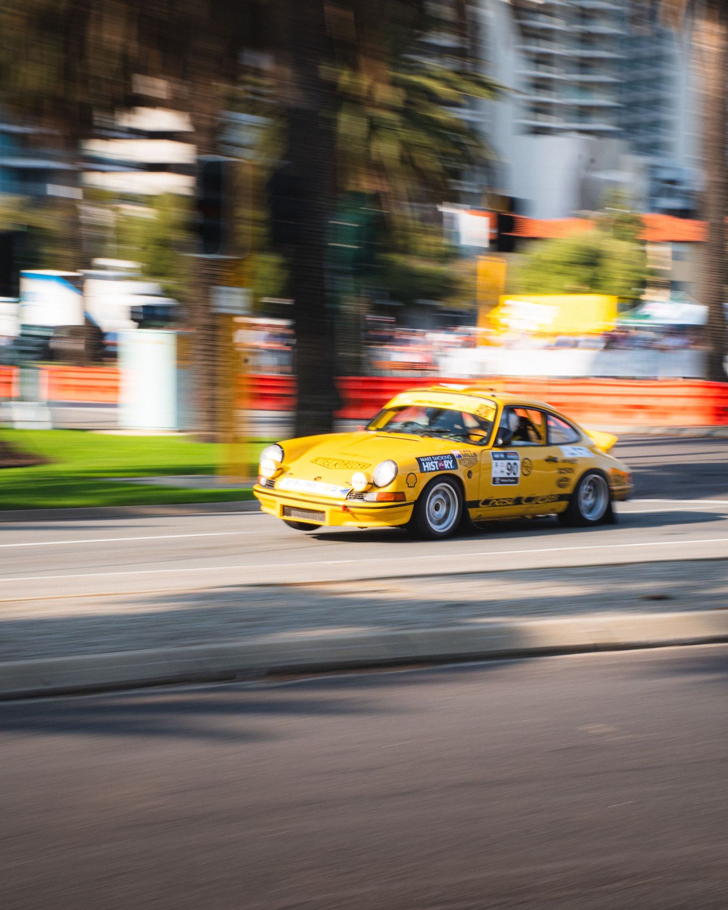 Yellow vintage Porsche 911 racing car captured in motion on street circuit.