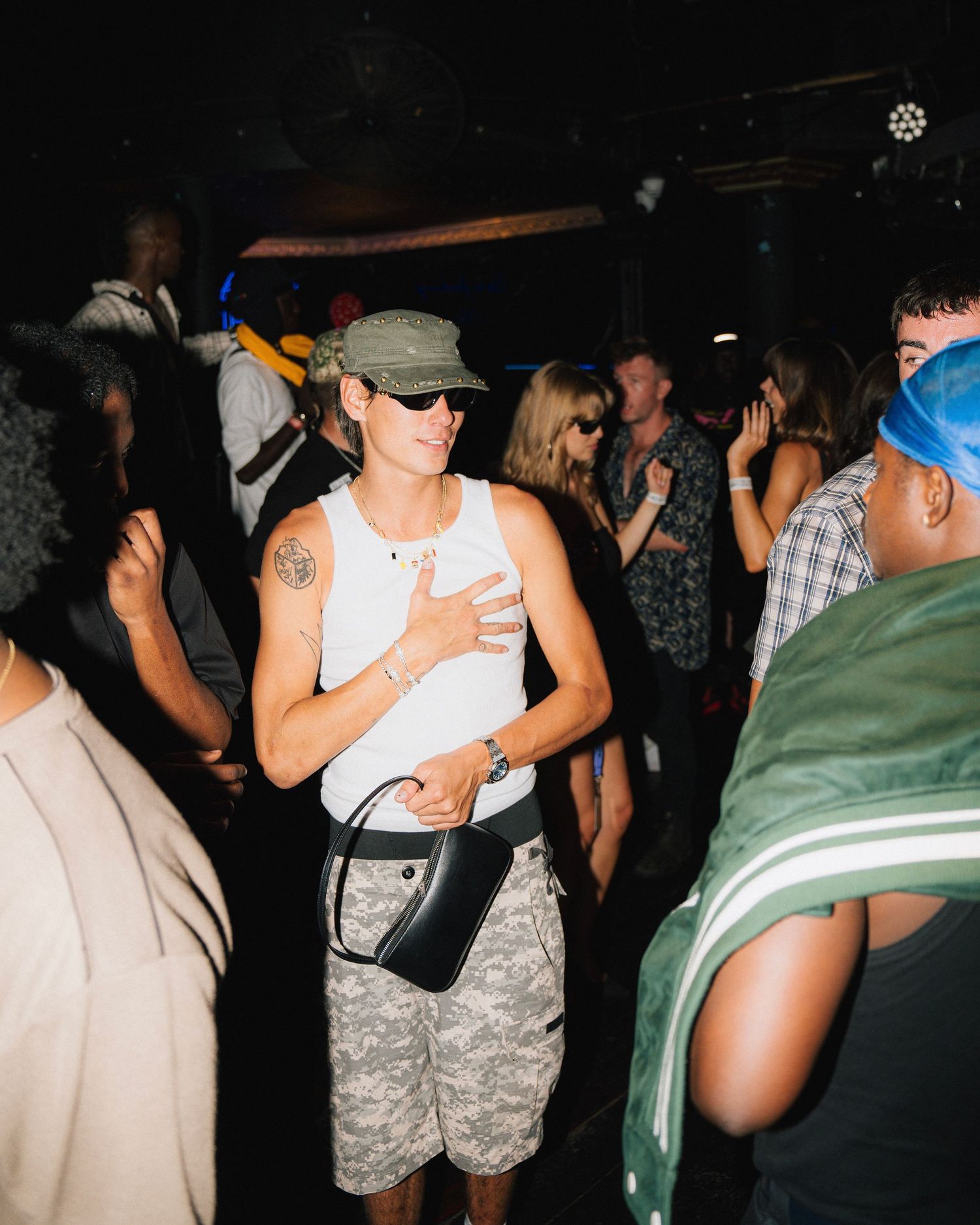 Casual scene of people mingling at night event with person in tank top and camo shorts.