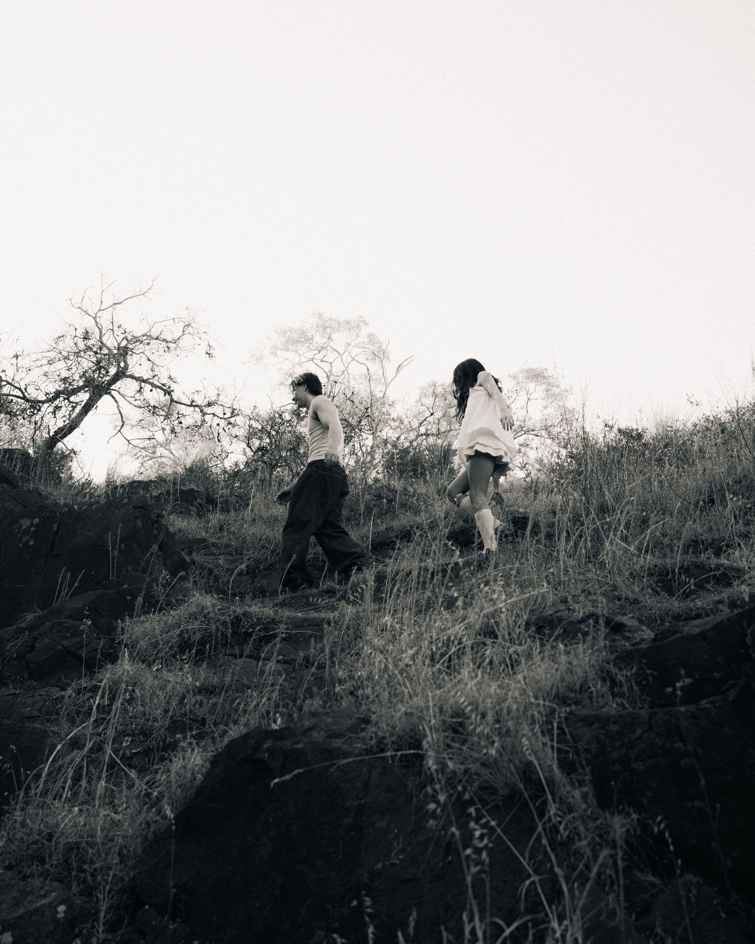 People climb a grassy hillside on a misty day in black and white silhouette.