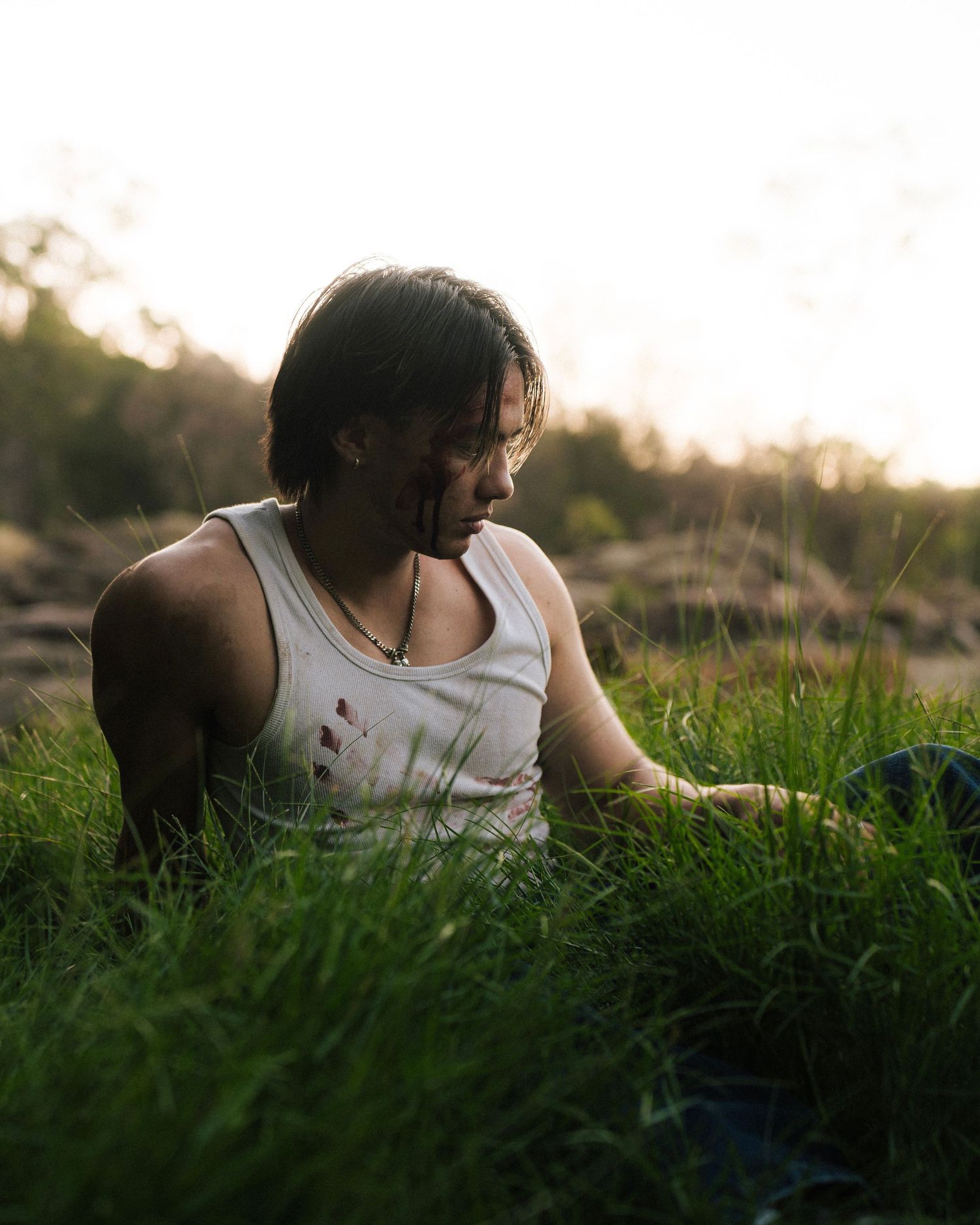 Person in white tank top sitting peacefully in tall grass during golden hour sunset lighting.