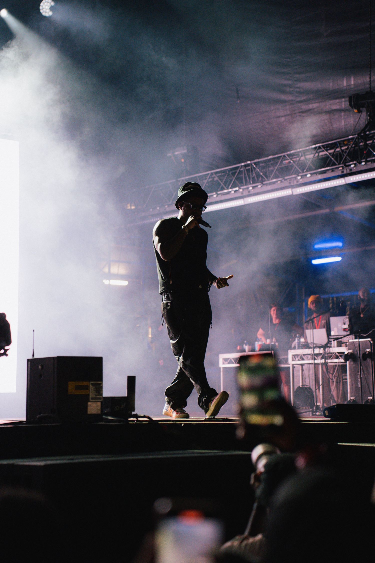 Silhouetted performer on stage surrounded by dramatic fog and theatrical lighting at a concert venue.