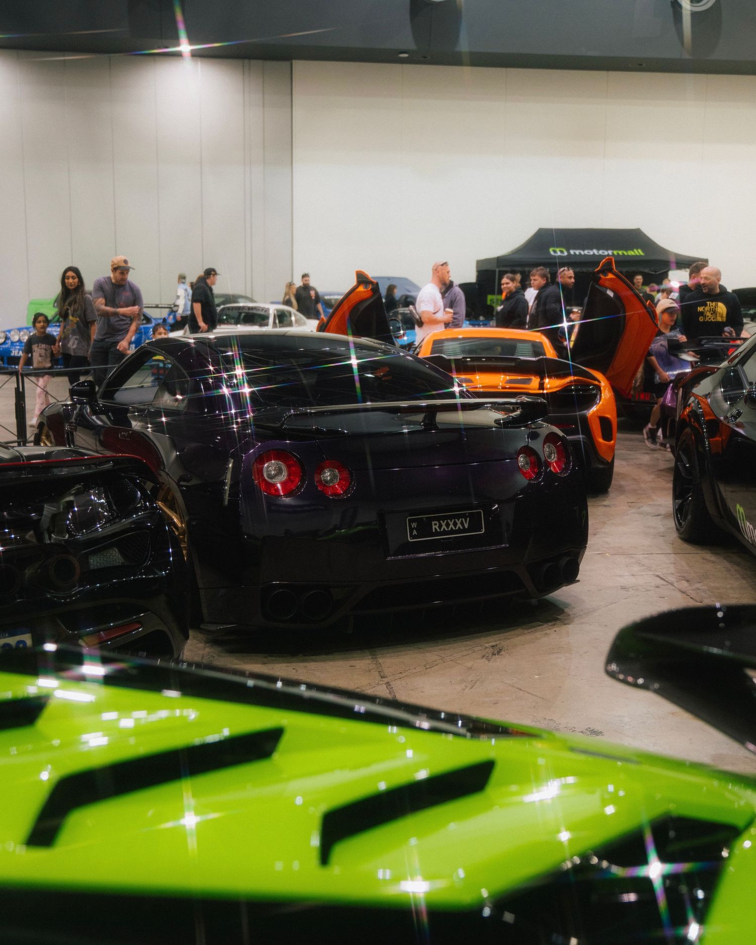 Black Nissan GT-R displayed at indoor car show surrounded by other performance vehicles.