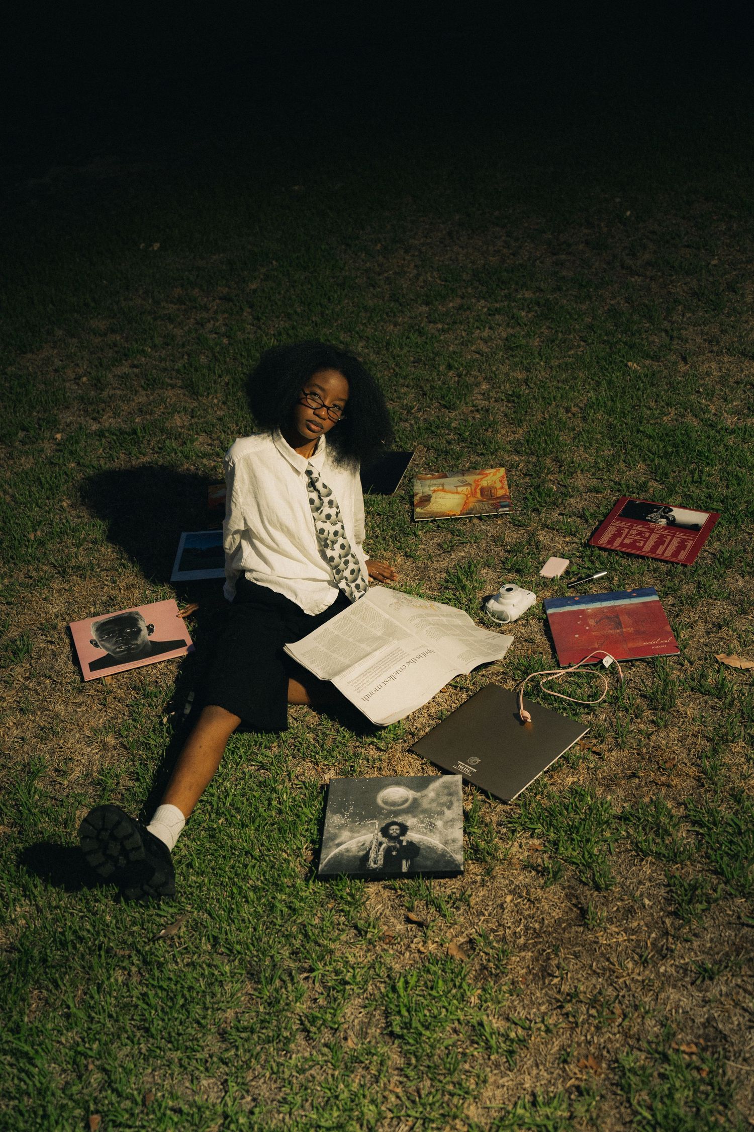 Student relaxing on grass surrounded by books and vinyl records in vintage style photography.