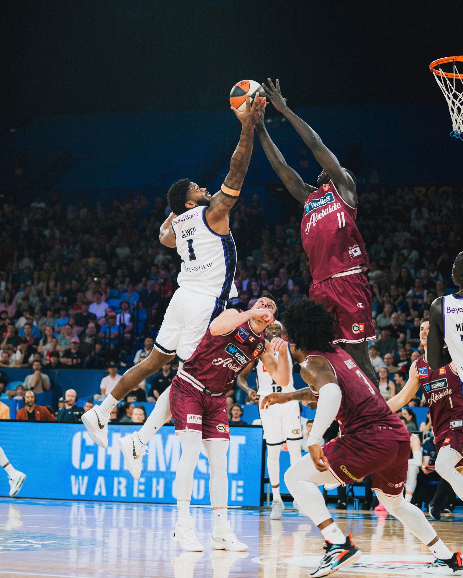 Two basketball players jump high to battle for possession of the ball.