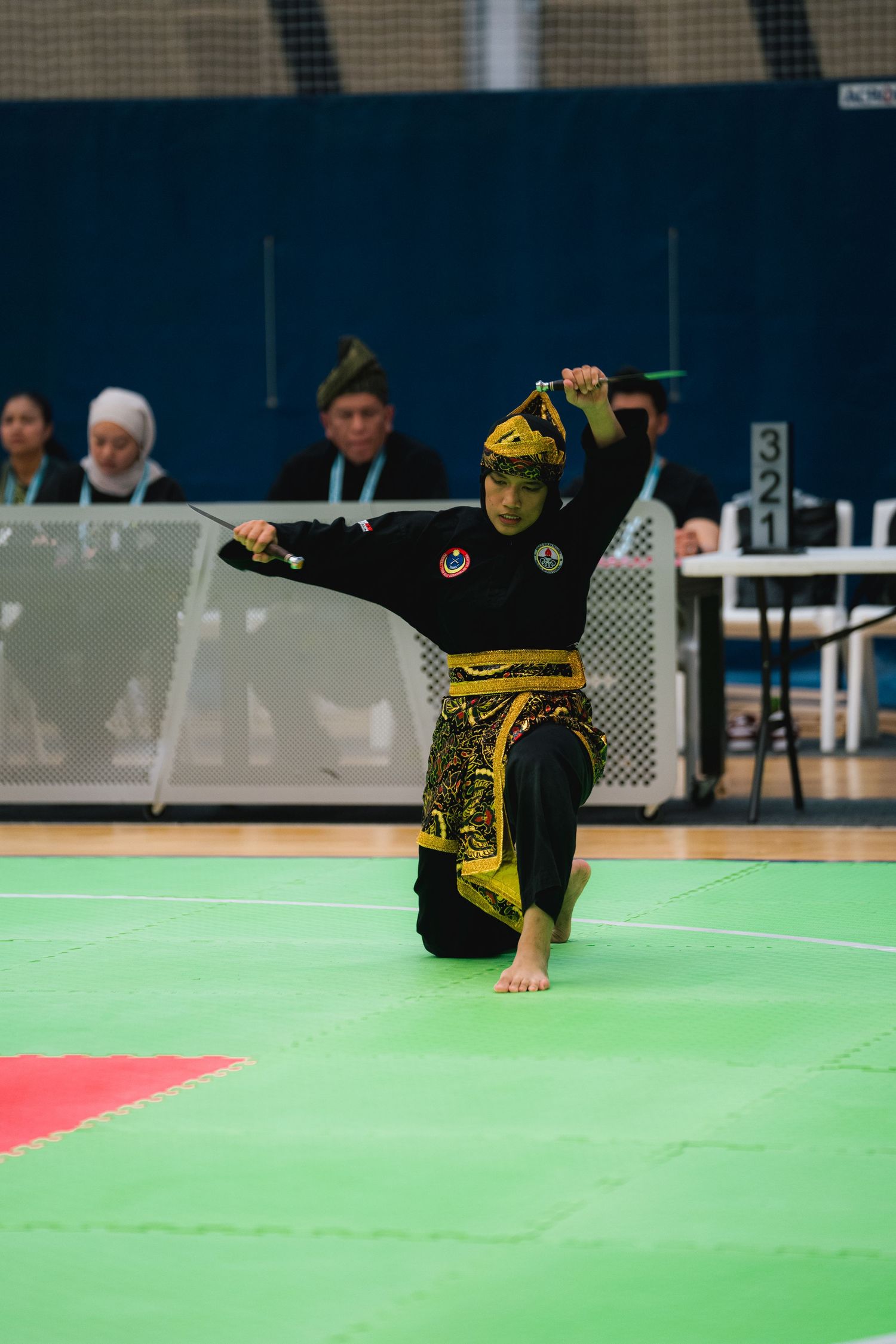 Martial artist in yellow and black traditional costume performs dynamic moves during competition.