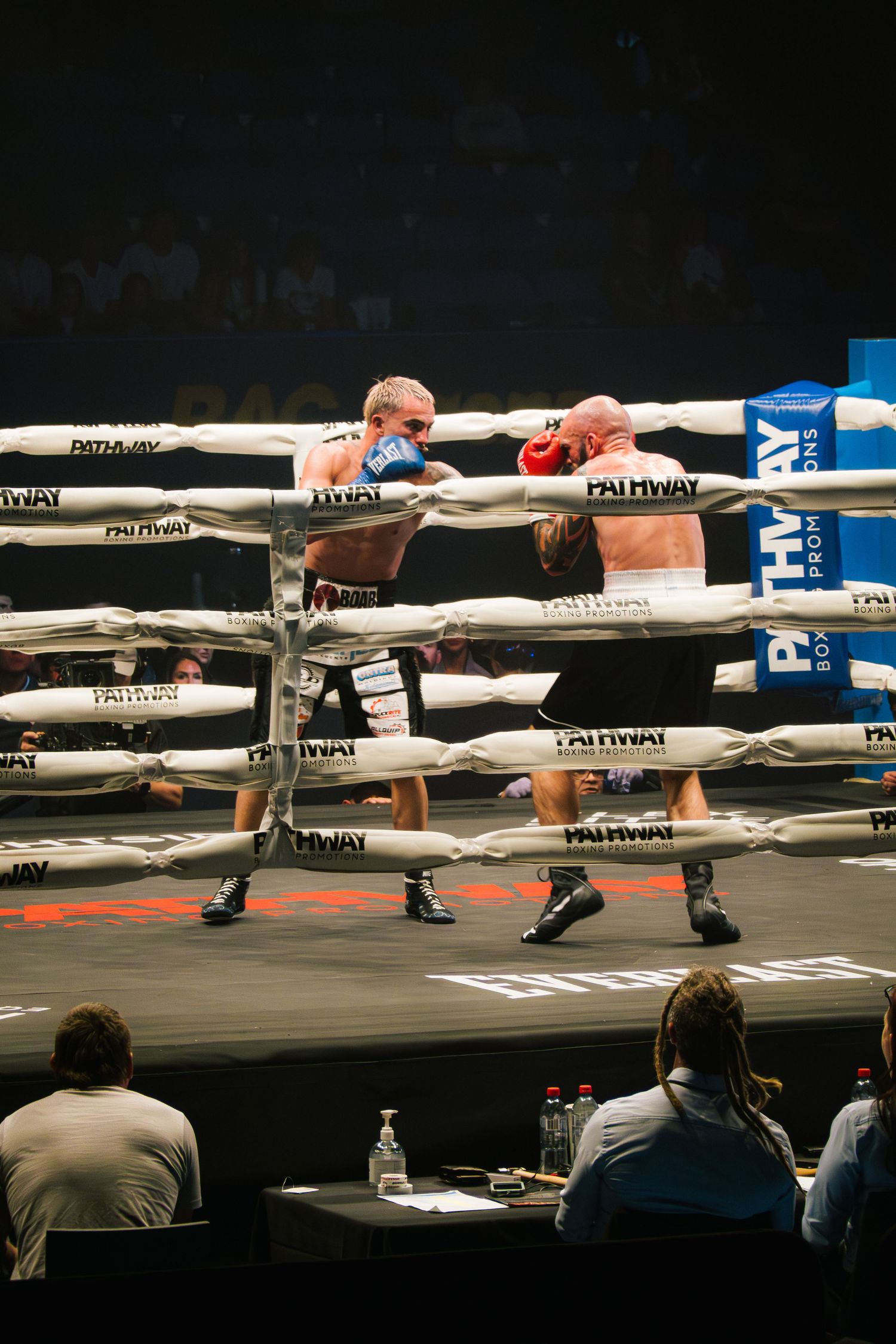 Two boxers exchanging punches through the white ropes of a boxing ring during a match.