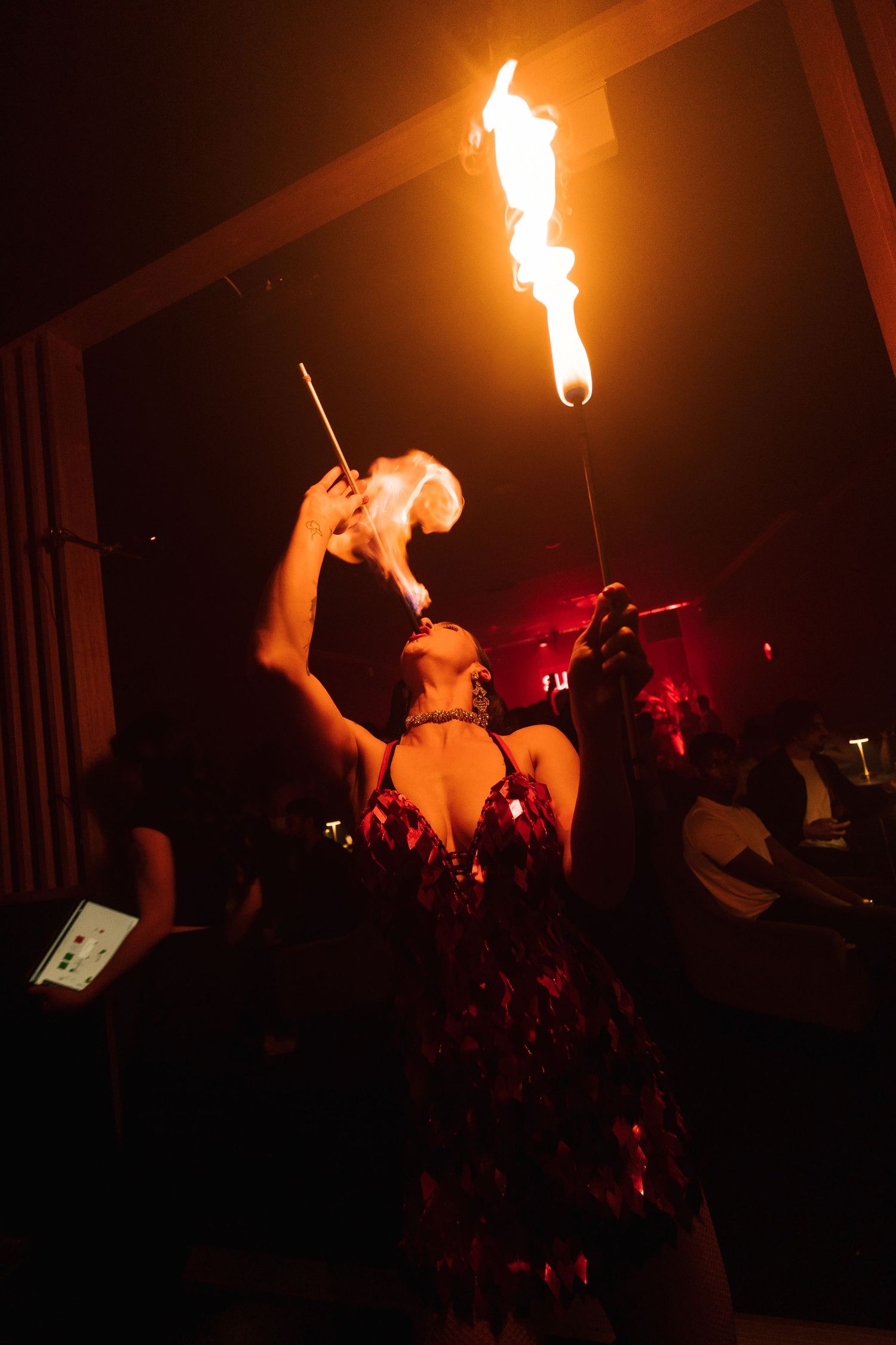 Fire performer breathes flames into the dark during an energetic stage performance with red lighting effects.