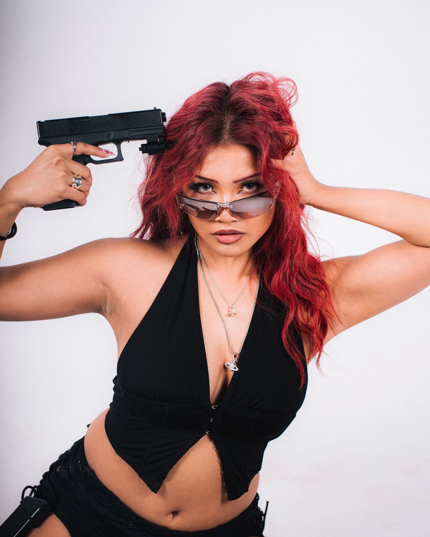 Edgy fashion photo of model with red hair in black top posing with prop gun.