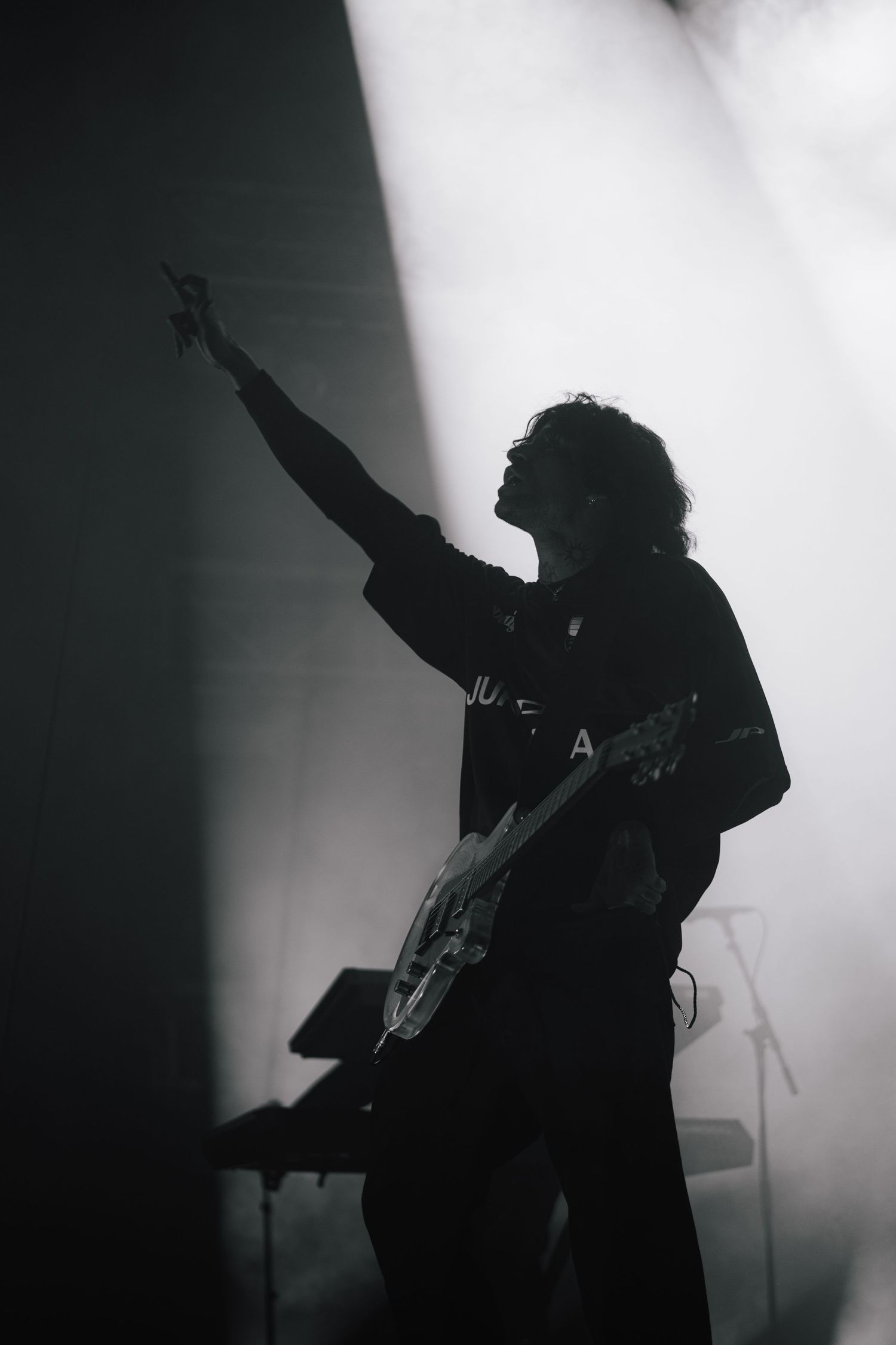 A silhouetted musician performs on stage with outstretched arm amid dramatic lighting and fog effects.