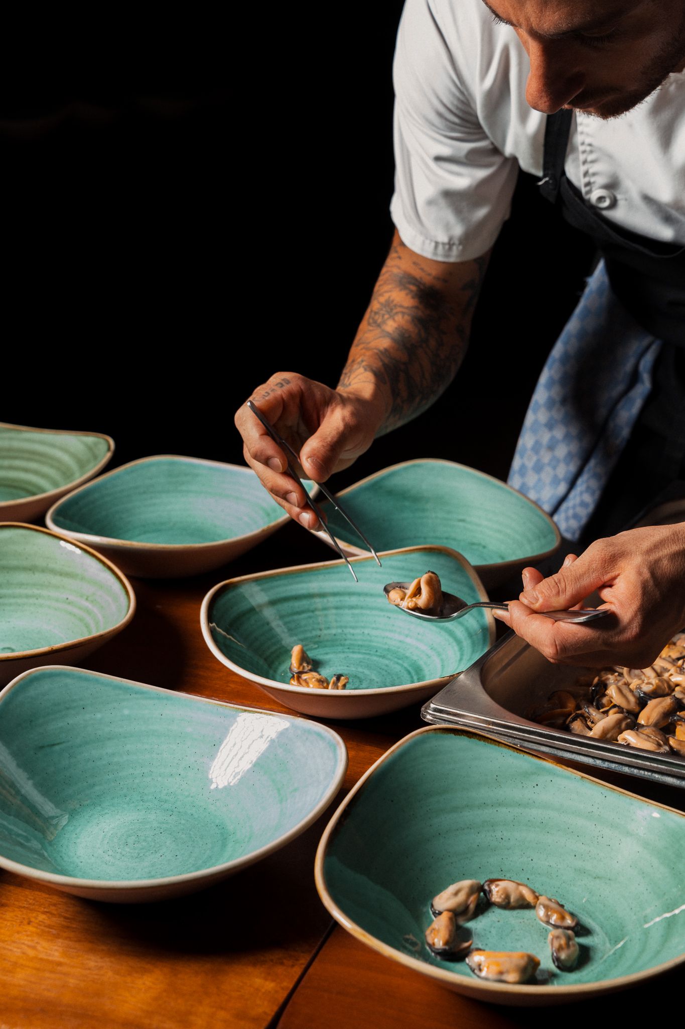 Chef plating dishes on turquoise ceramic plates at a wooden dining table.