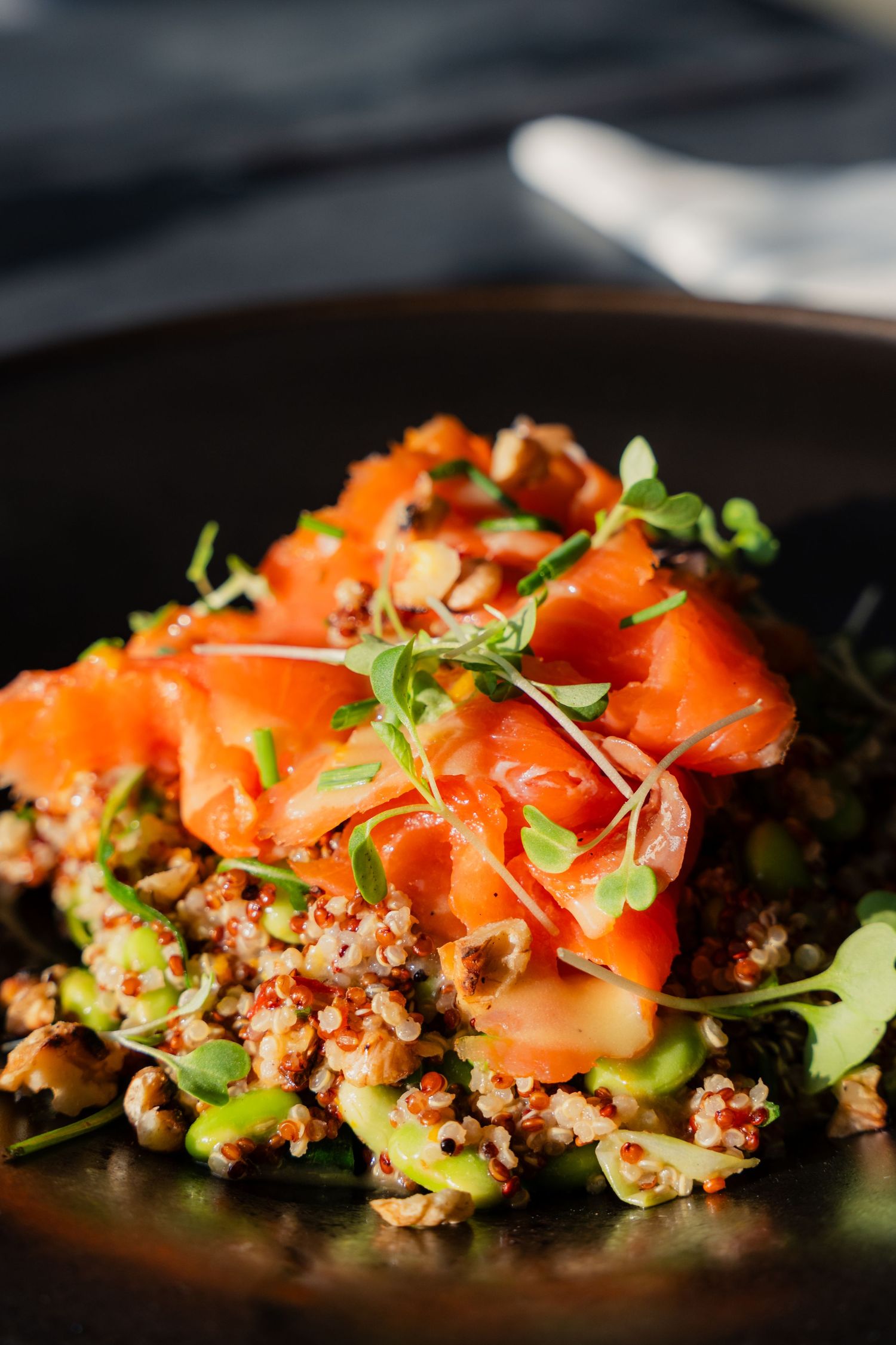 Fresh salmon sashimi served over a quinoa and vegetable medley on black plate.
