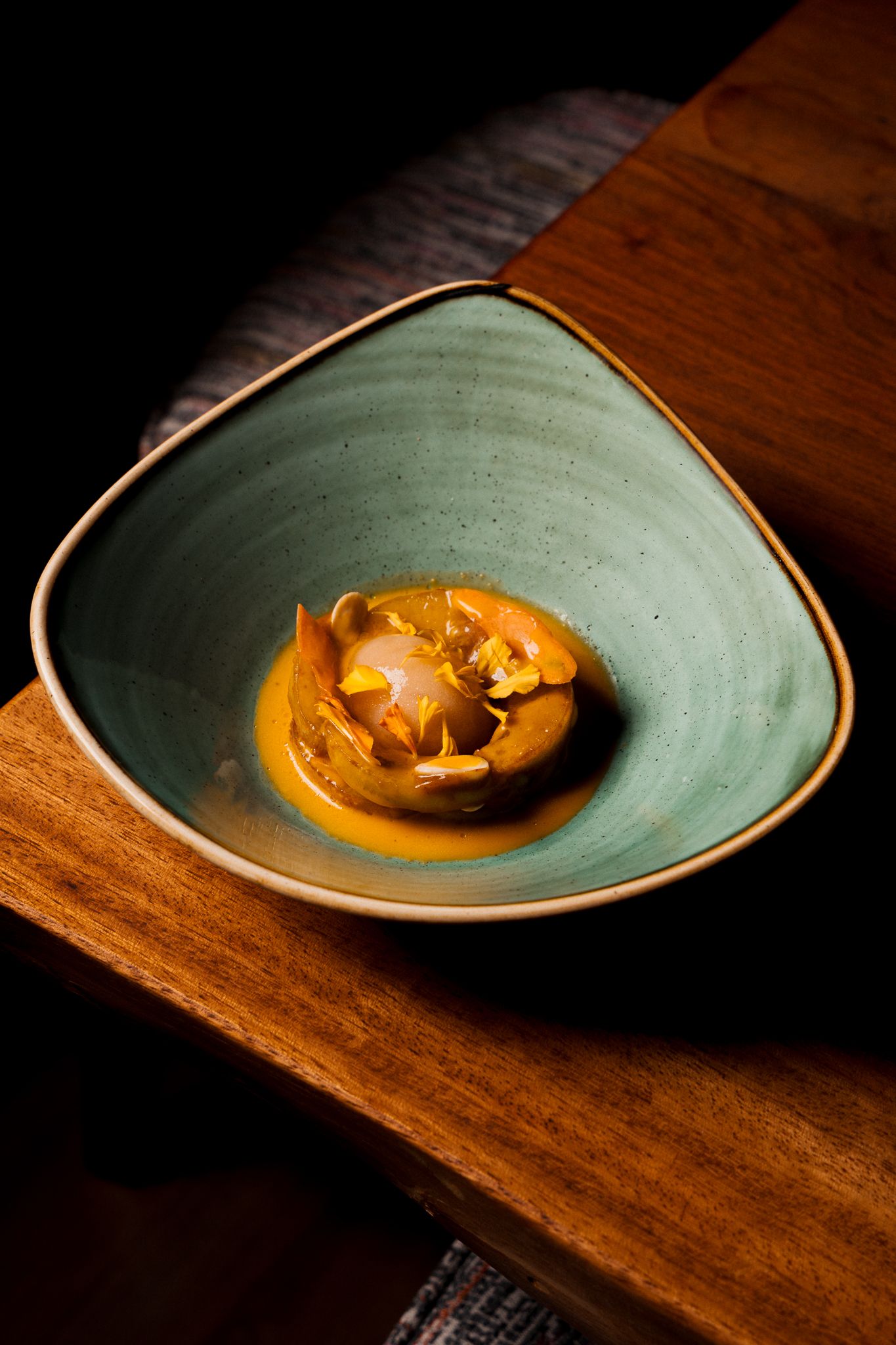 A beautifully plated dish on a sage green ceramic plate rests on a rustic wooden surface in dramatic lighting.