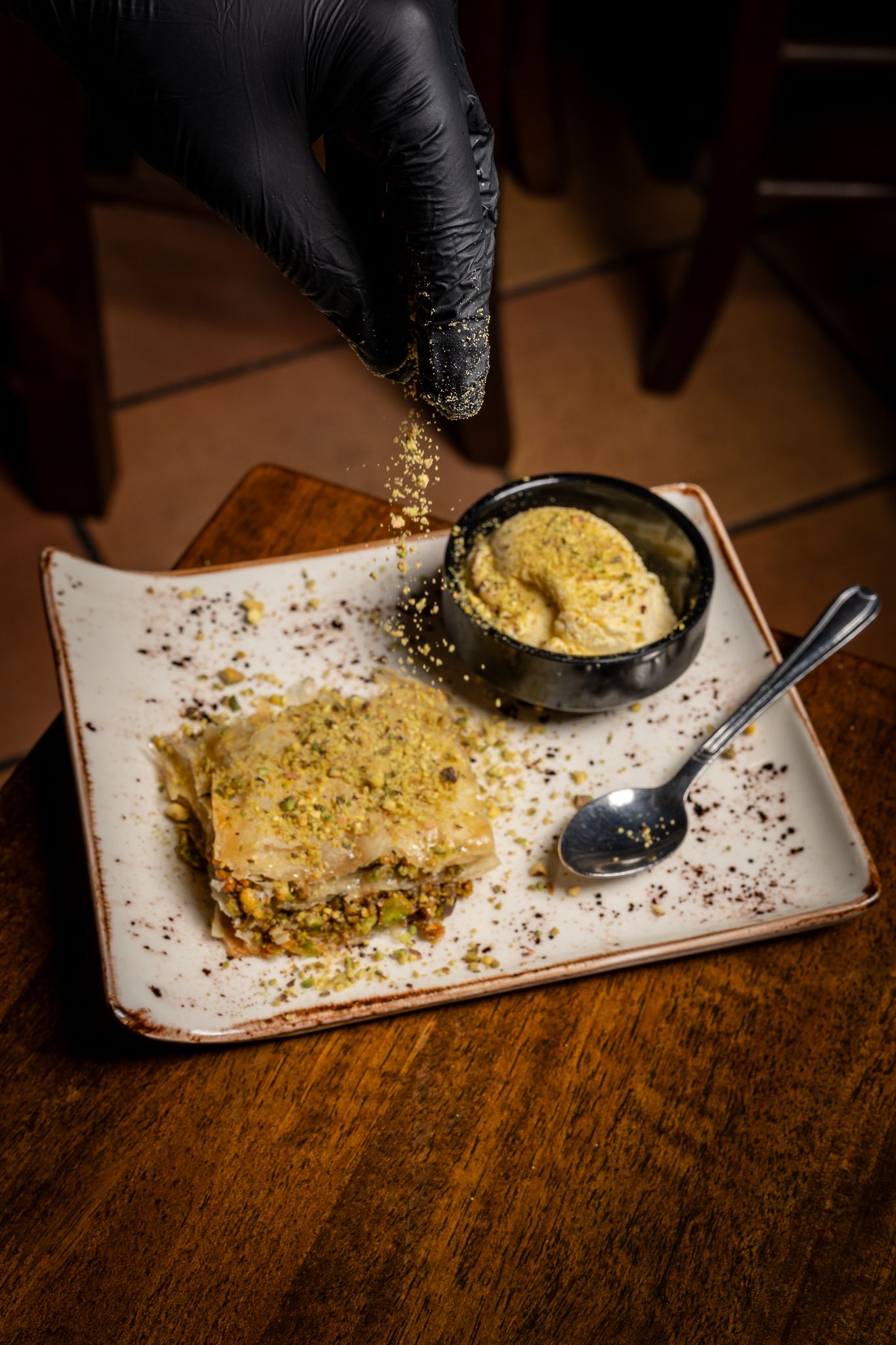 Sequential shots of a chef garnishing a pale yellow dish with seasonings on a white rectangular plate.