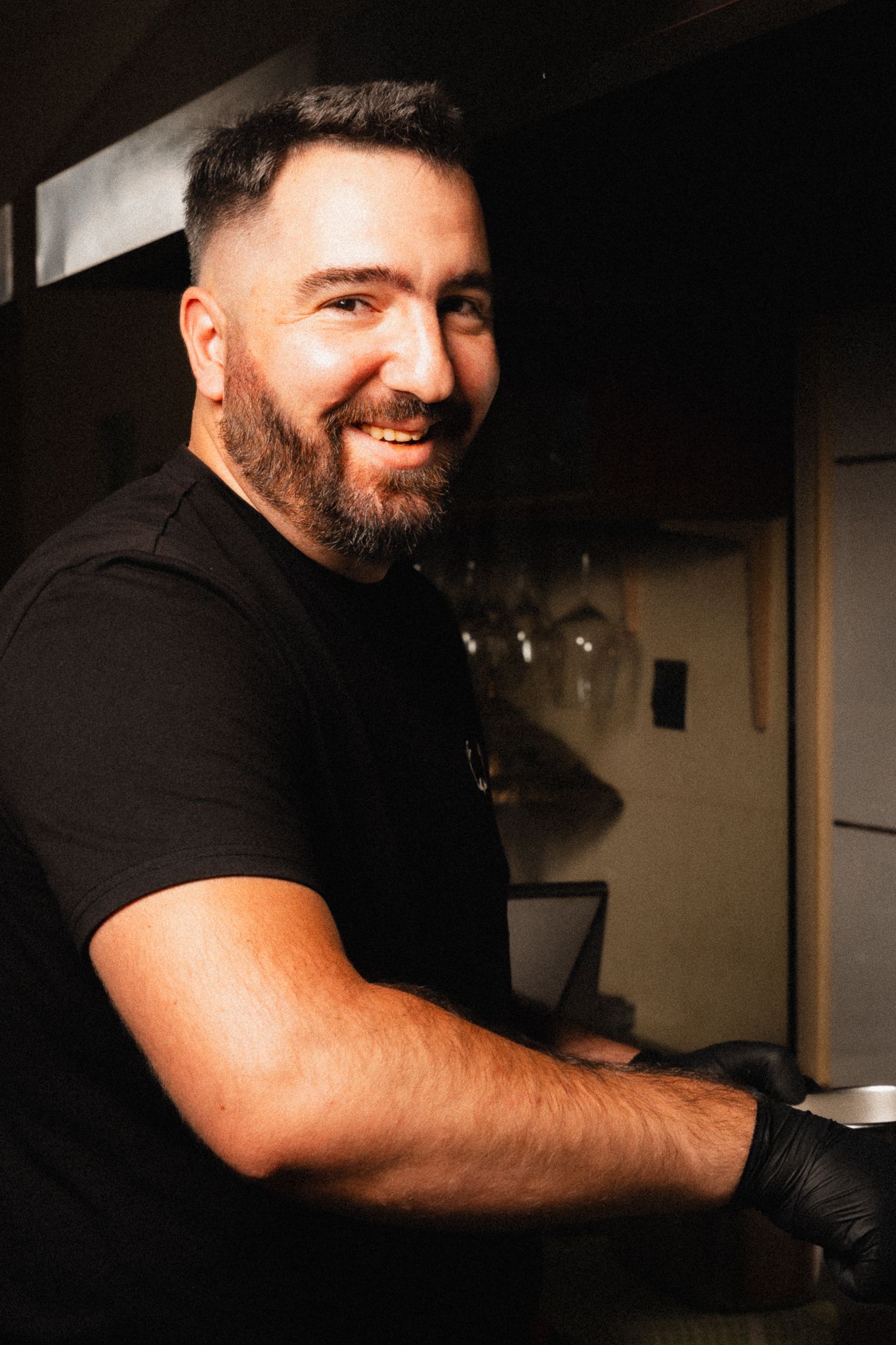 Chef wearing black shirt and gloves working in a commercial kitchen.