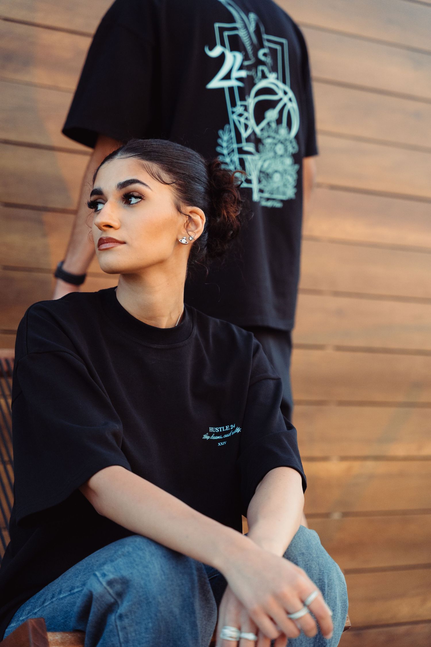 Person in black sweatshirt sitting against wooden wall with graphic t-shirt display.