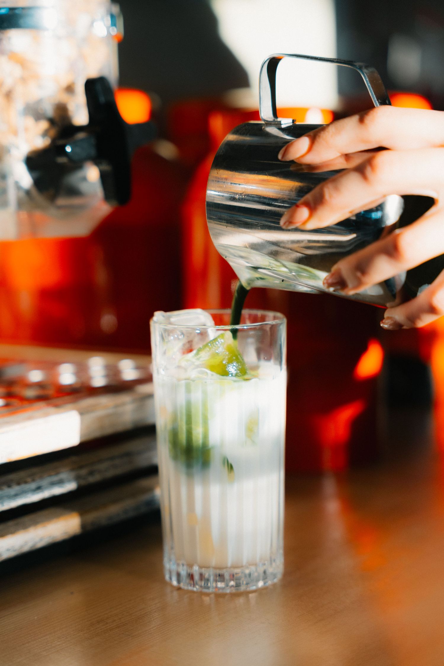 Pouring a clear liquid into a tall glass with ice and mint garnish.
