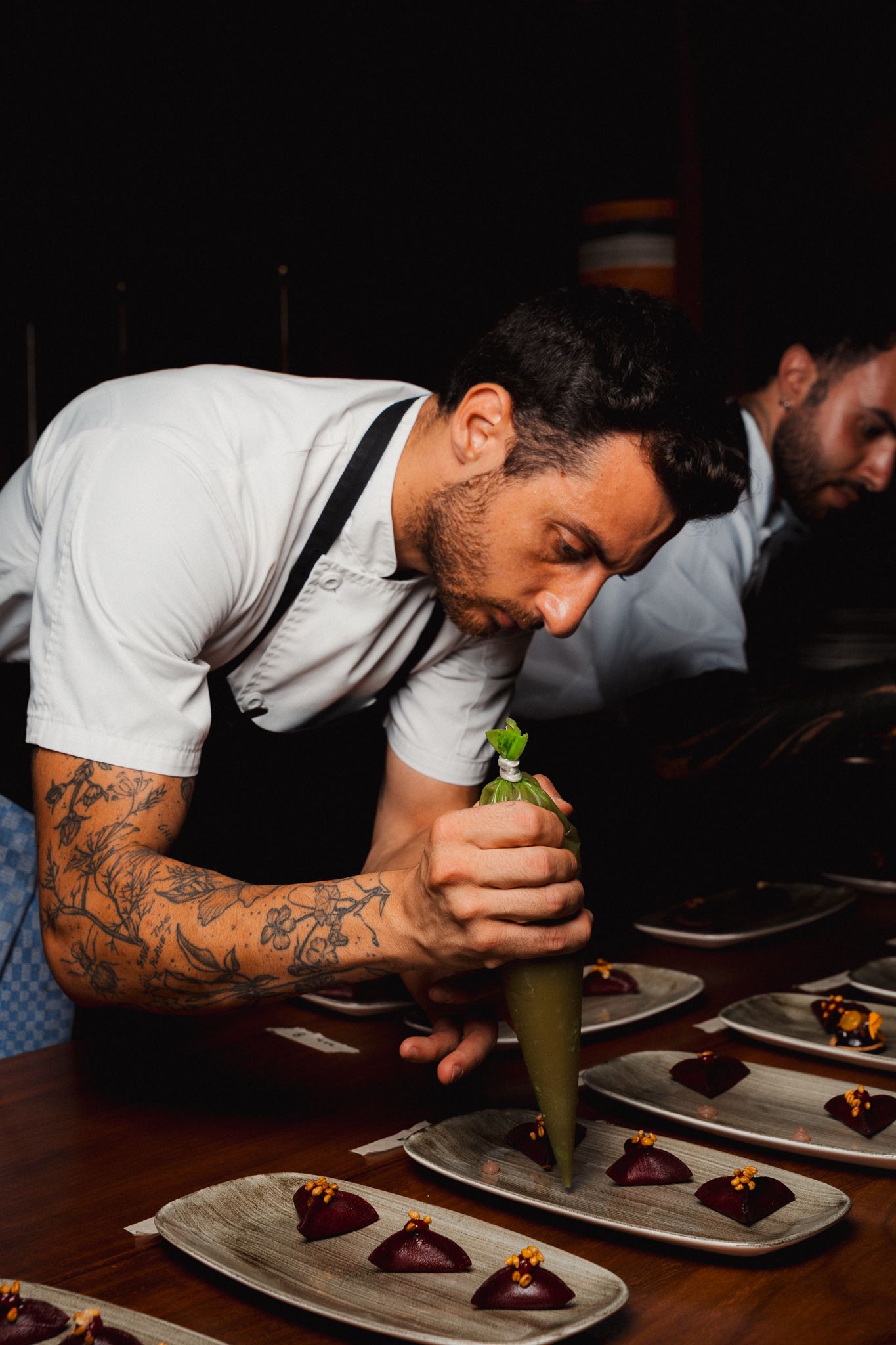 Chef carefully plates dishes in a dimly lit restaurant, focusing on precise culinary presentation.