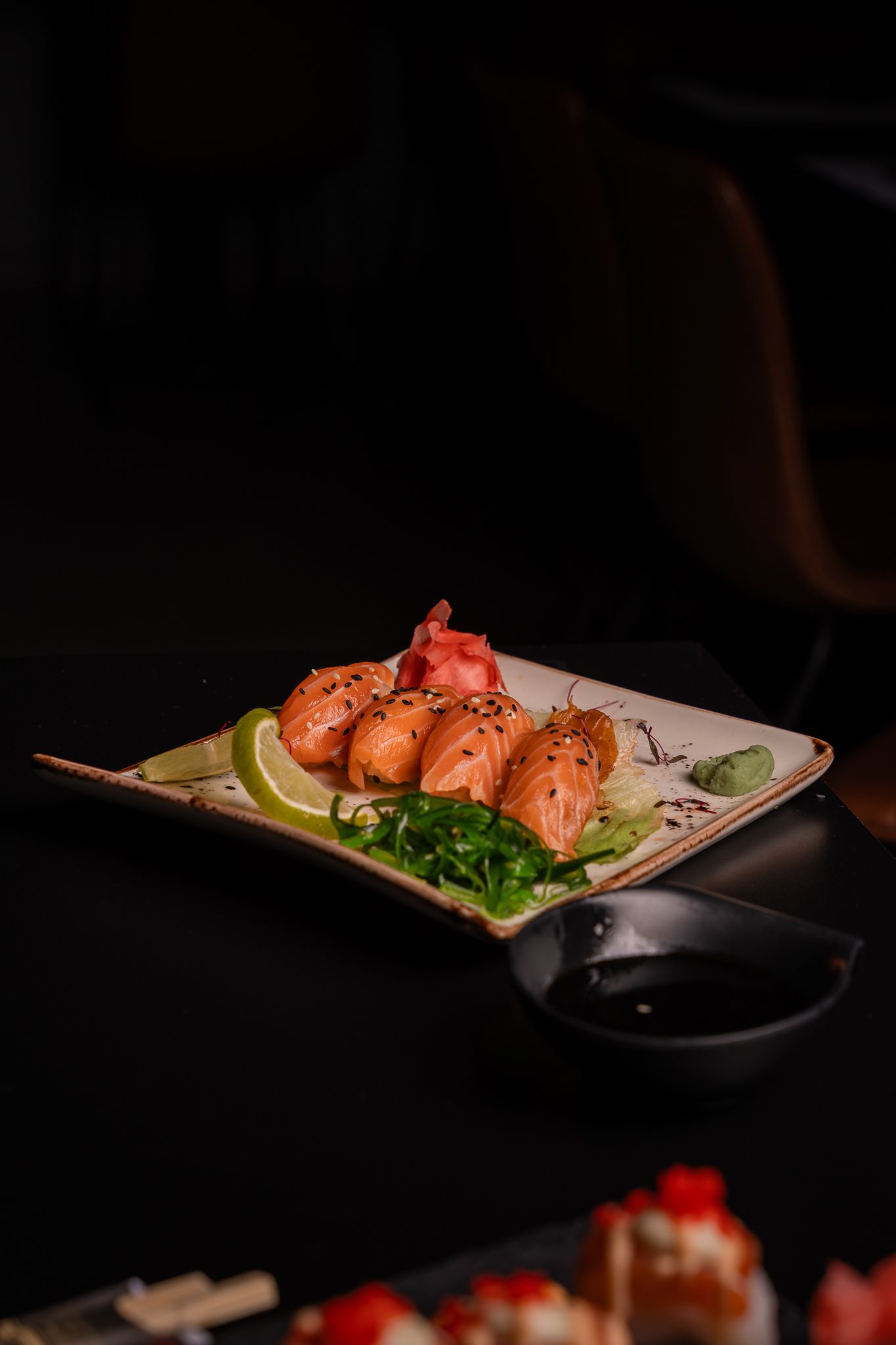Artistic presentation of sushi rolls on a white plate with garnish in dramatic dark lighting.