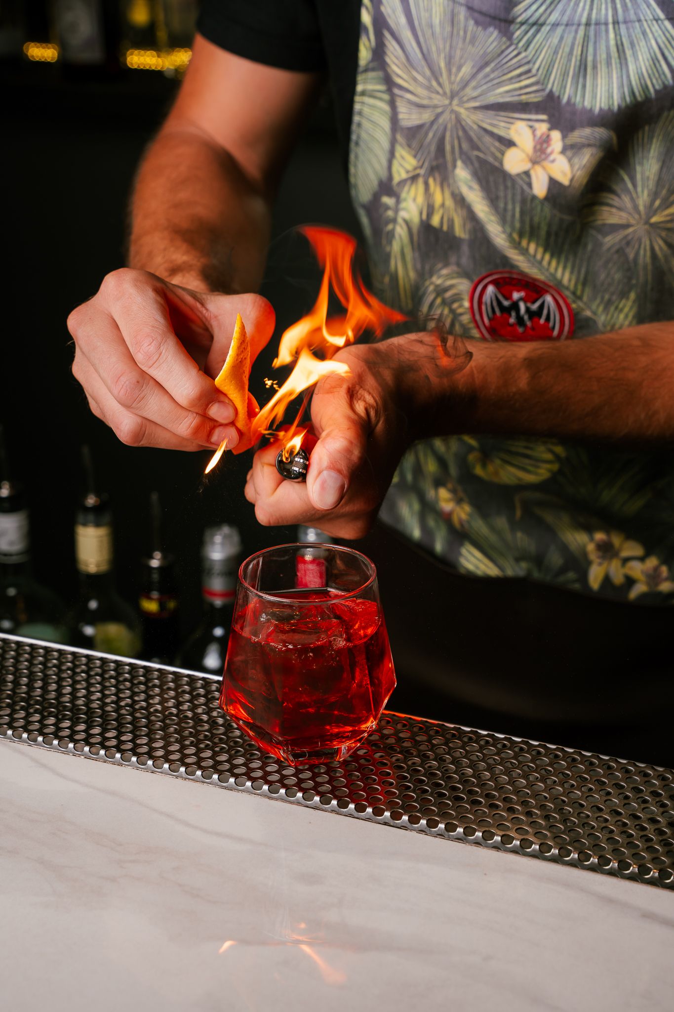 Bartender garnishing red cocktails with orange peel flames in sequential action shots on a bar mat.