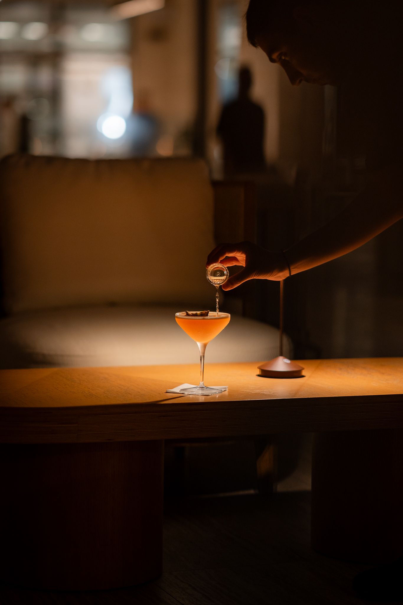 A sequence of cocktail making shots showing orange drinks being poured into martini glasses on a wooden surface.