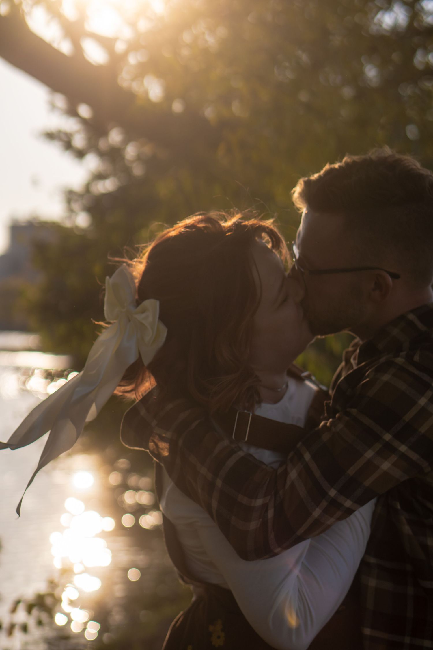 Silhouetted couple embracing in golden sunset light through trees.