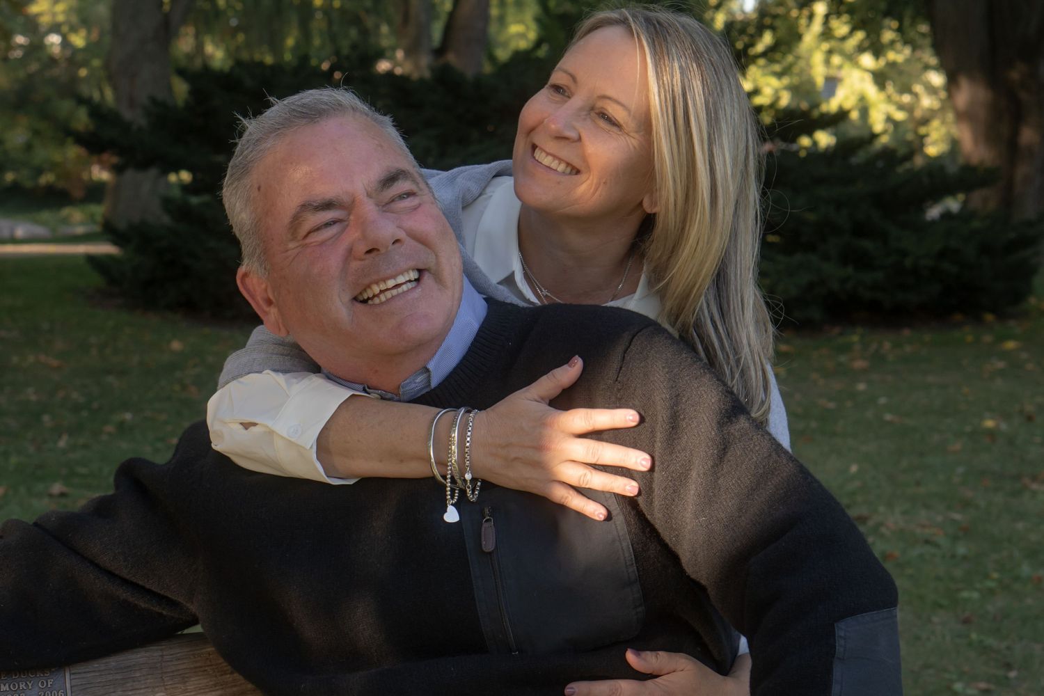 A joyful couple shares laughter and embraces in a sunny outdoor garden setting.