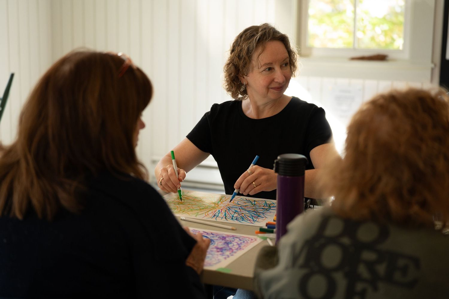 Students sit at tables in a classroom working on assignments while an instructor provides guidance and support.