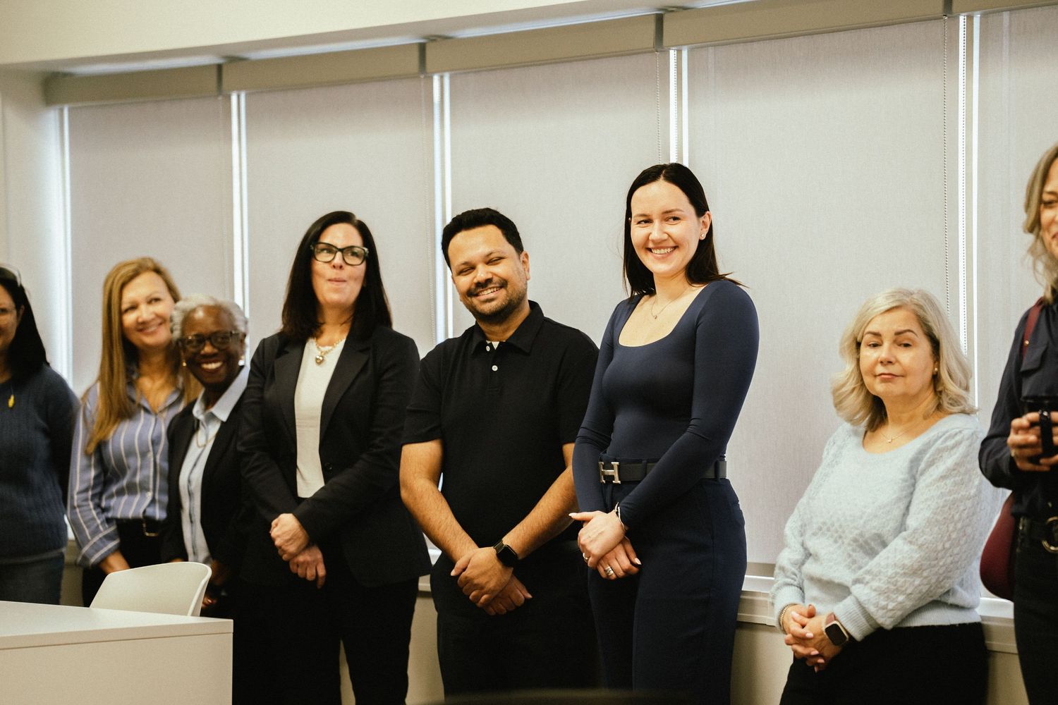 A diverse group of professionals stands together in a line against a white wall during a business meeting.