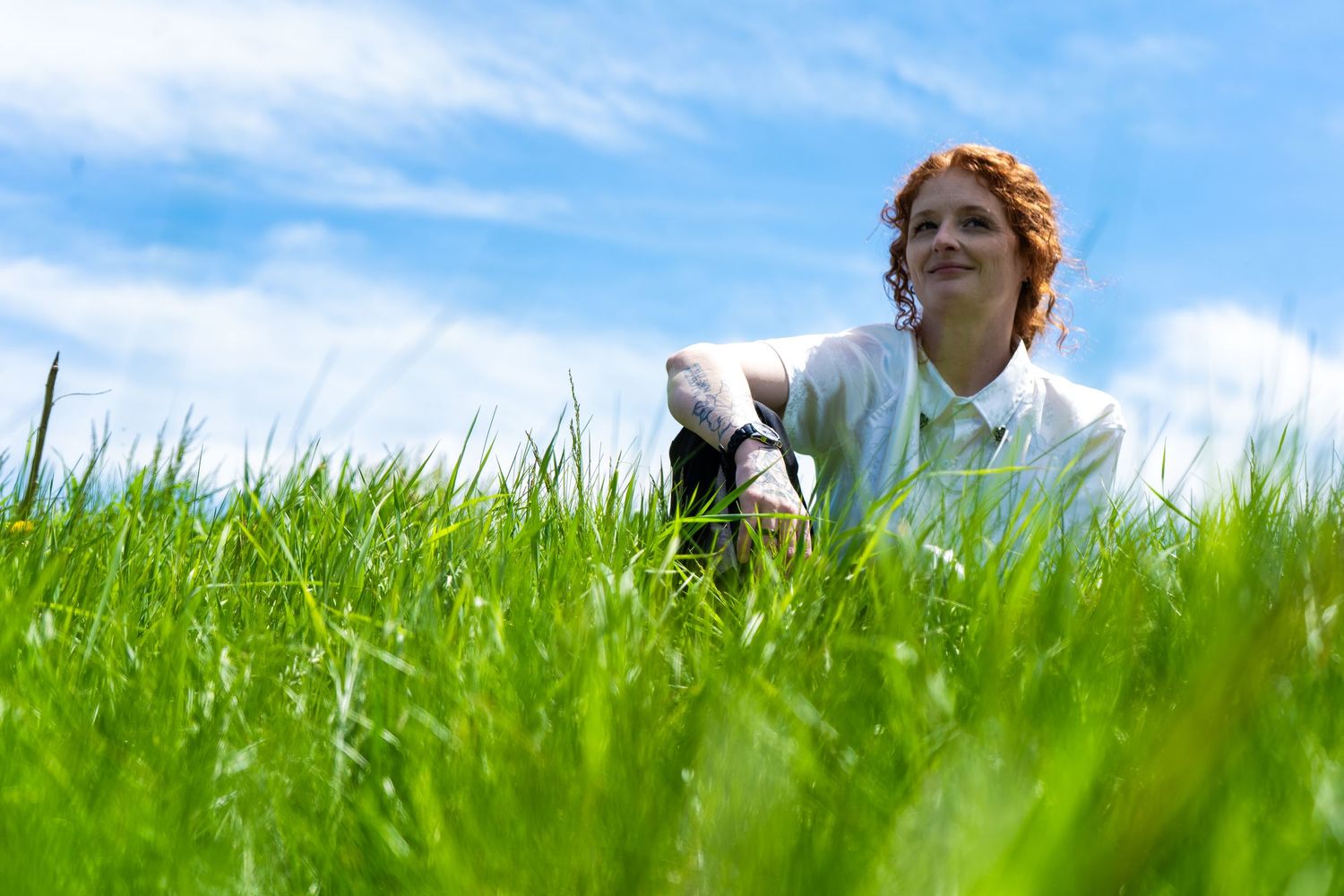 Someone relaxes in a vibrant green grass field on a sunny day with blue sky overhead.