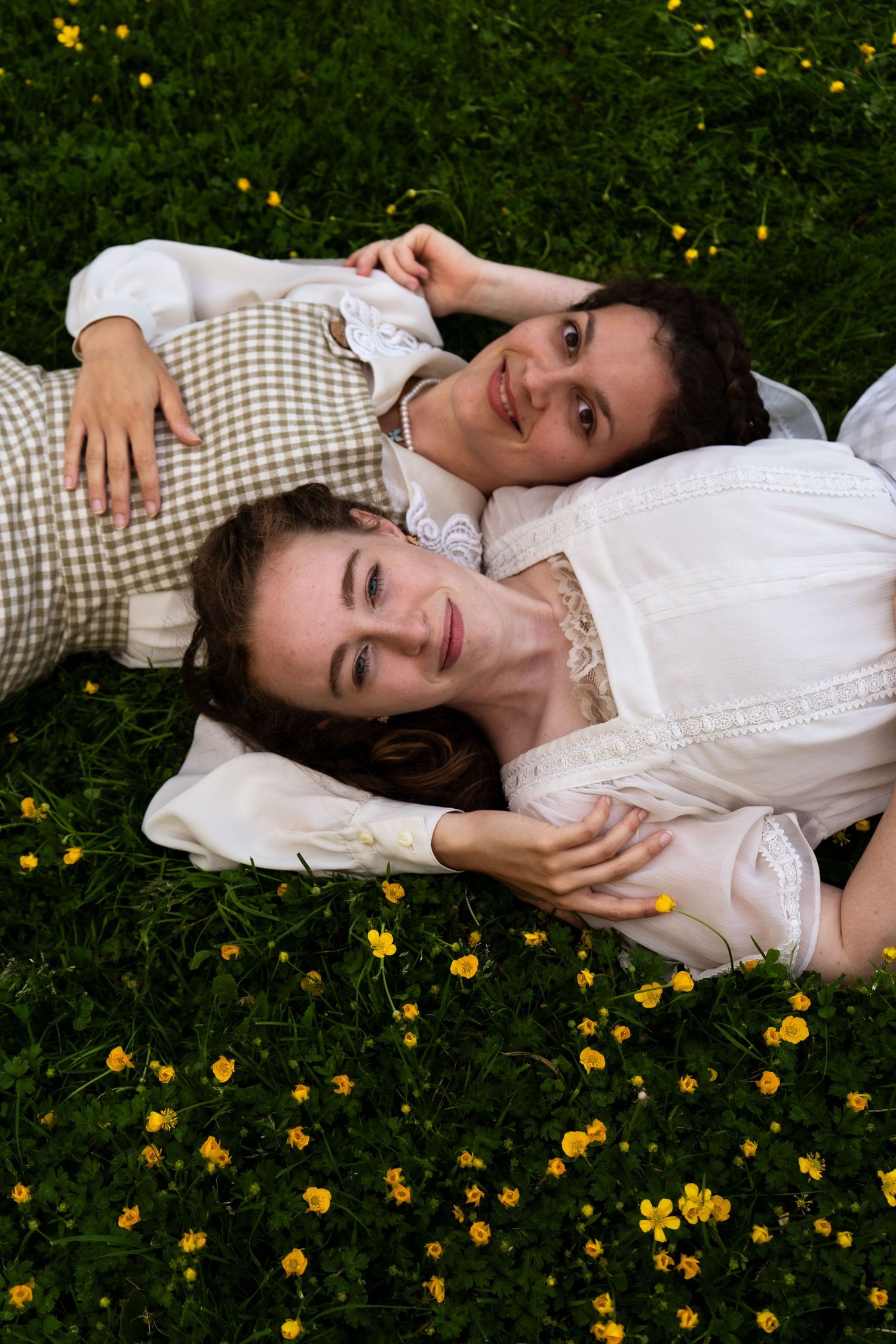 A person in a white dress lying in a field of yellow wildflowers with a gingham blanket.