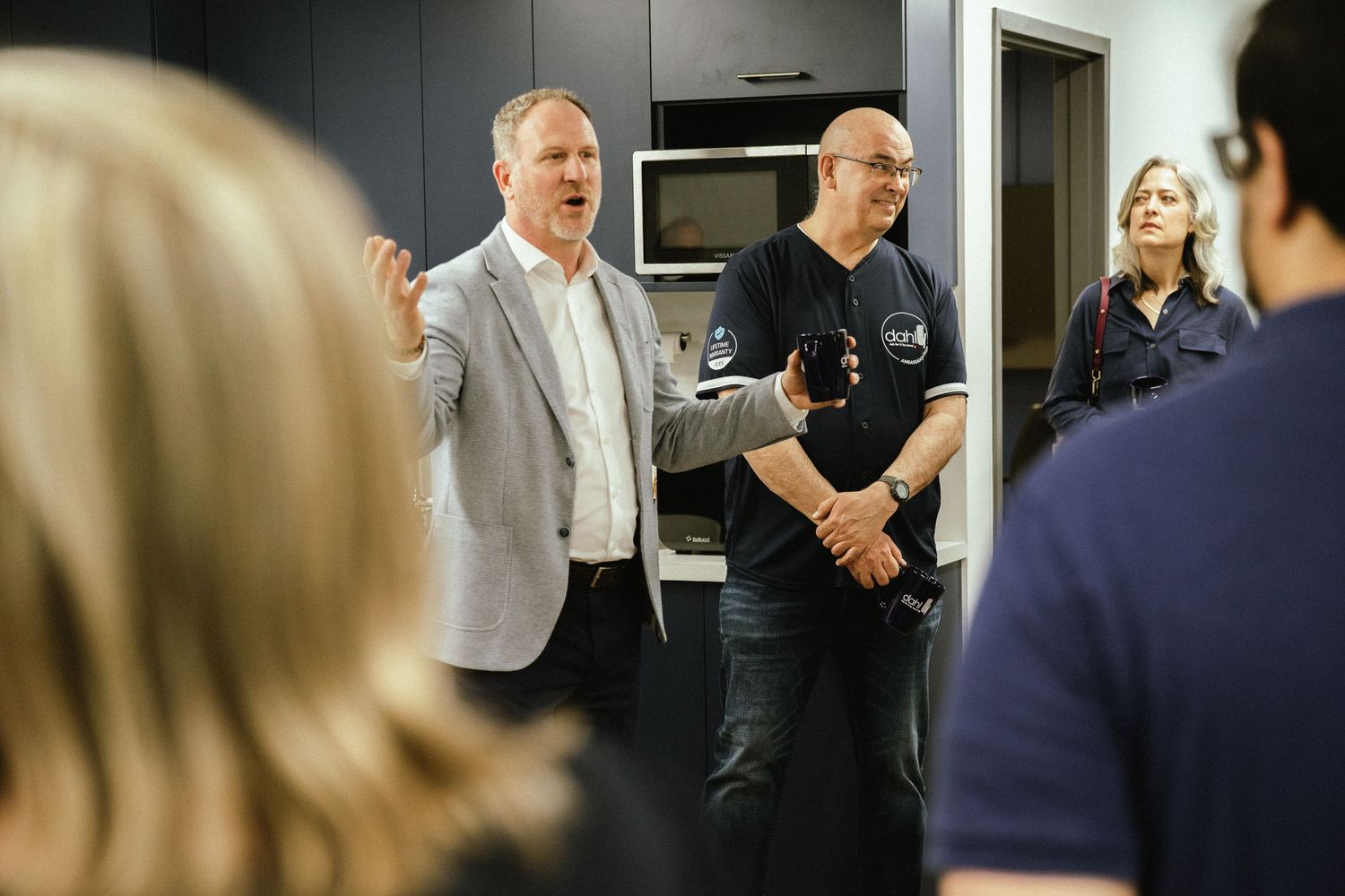 Business professionals engaged in discussion in a modern office kitchen setting.