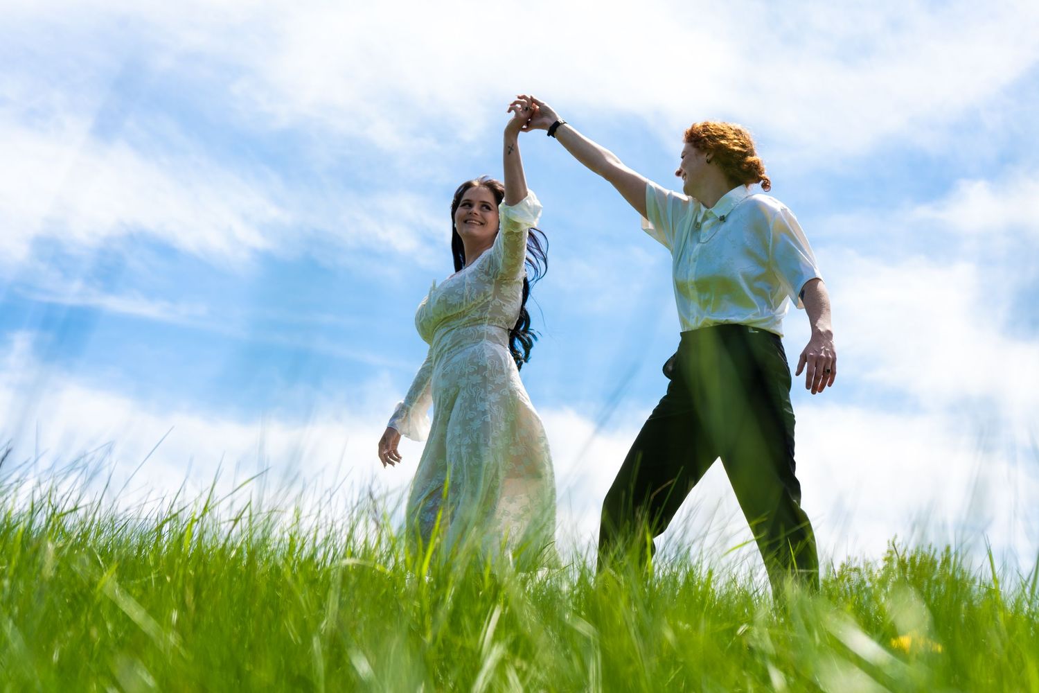 couple walk and hold hands in field of grass.