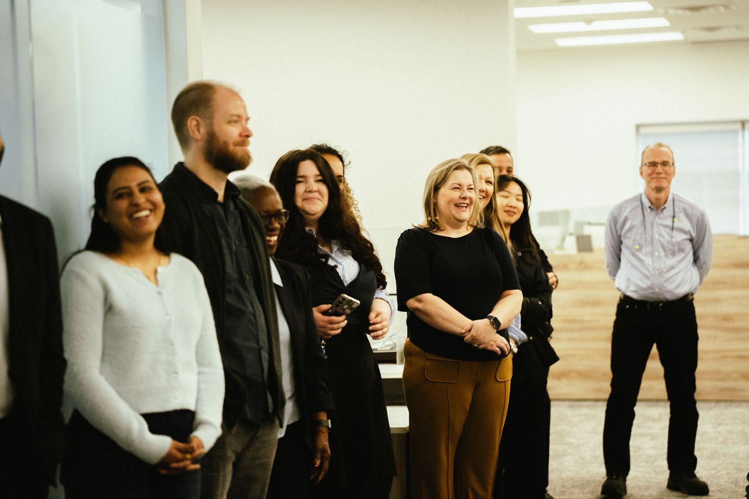 A group of professionals standing together in a bright office hallway during what appears to be a business meeting.