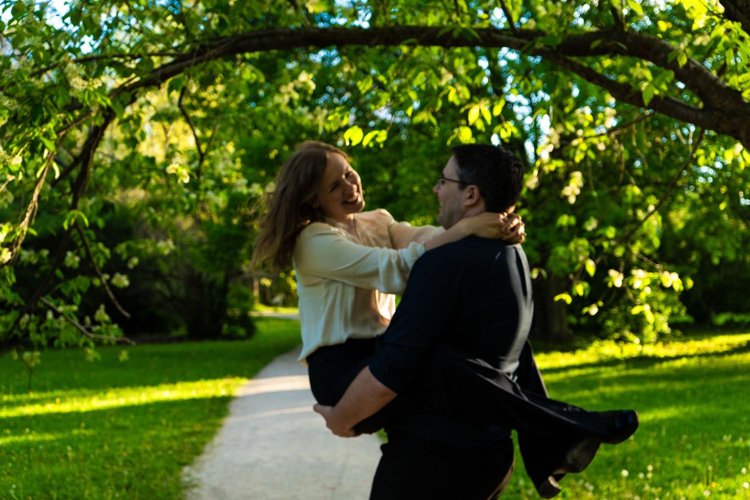 Two people dance together in a lush garden setting surrounded by green foliage and sunlight.