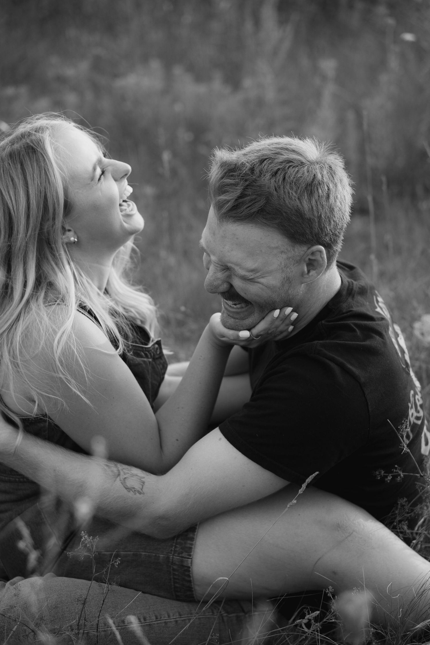 couple both laugh while sitting together in grass