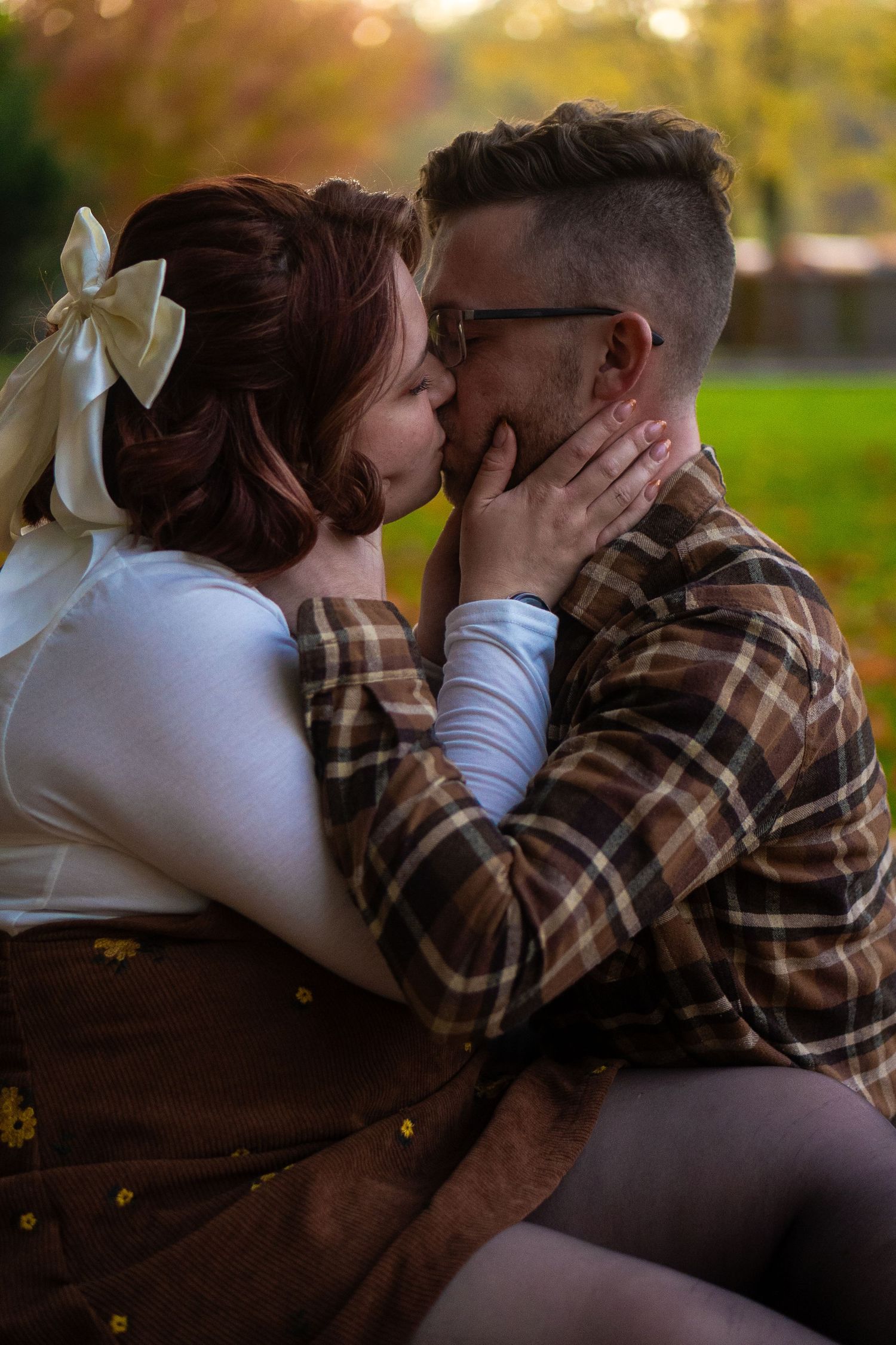 Intimate couple embracing on a park bench during golden hour with autumn colors in the background.