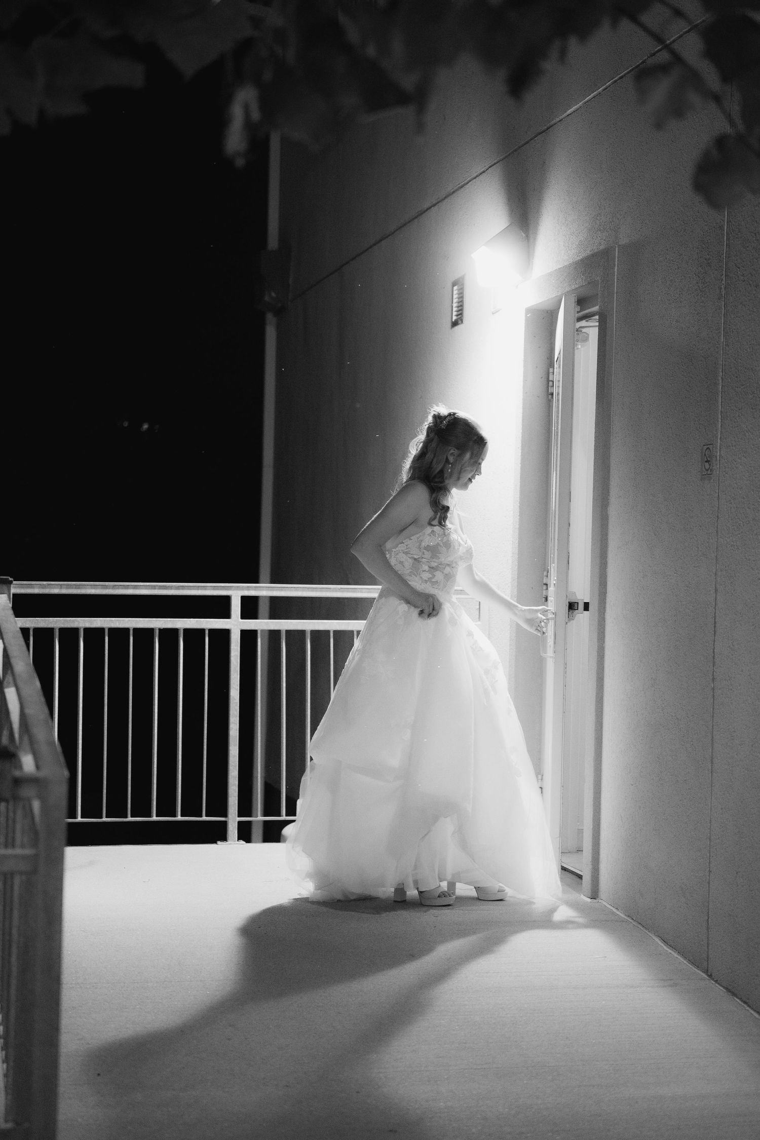 bride ins opening a door with light pooring down on here in black and white