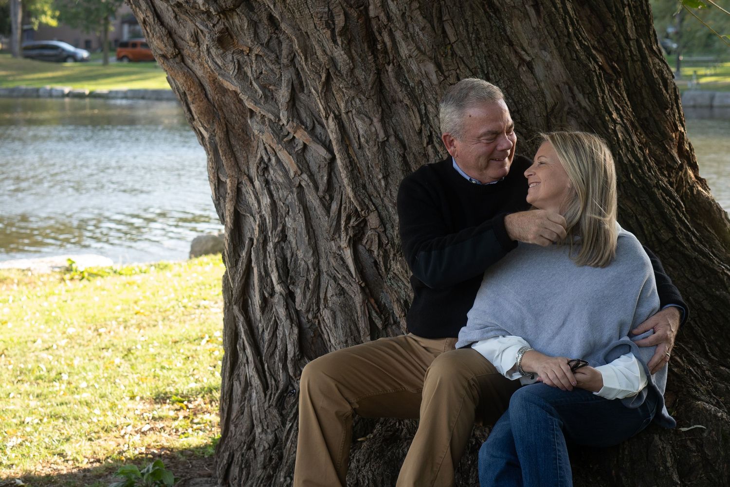 Couple sitting together outdoors under a large tree trunk on a sunny day.
