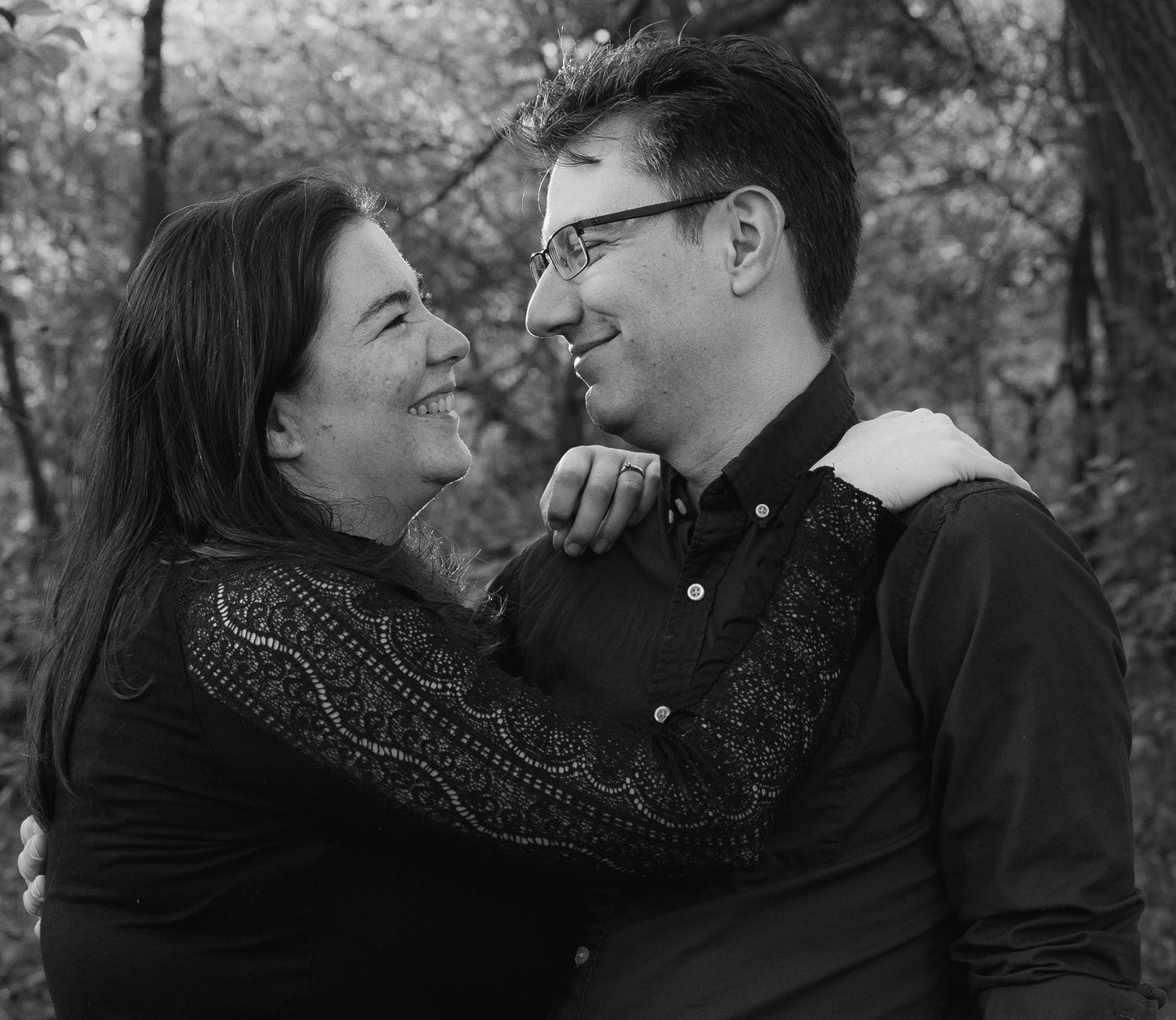 A couple in dark sweaters share a tender moment while embracing outdoors in black and white.