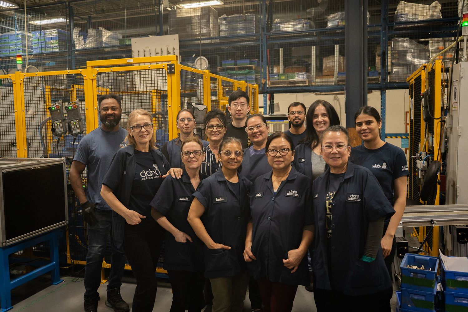 Manufacturing facility employees in navy blue uniforms stand together in front of industrial equipment for a group photo.