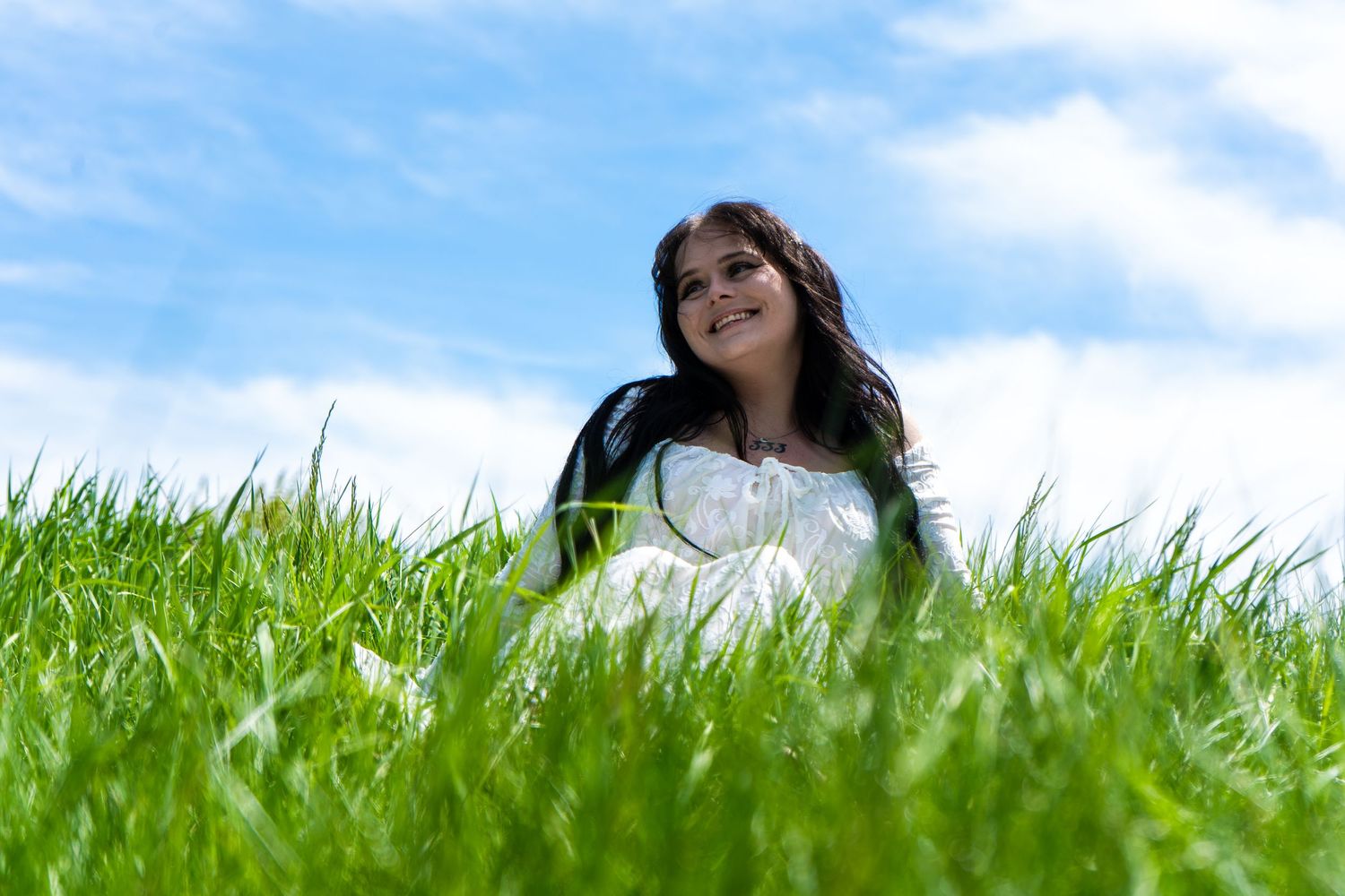 Person lying in a lush green grass meadow under bright blue sky on a sunny summer day.