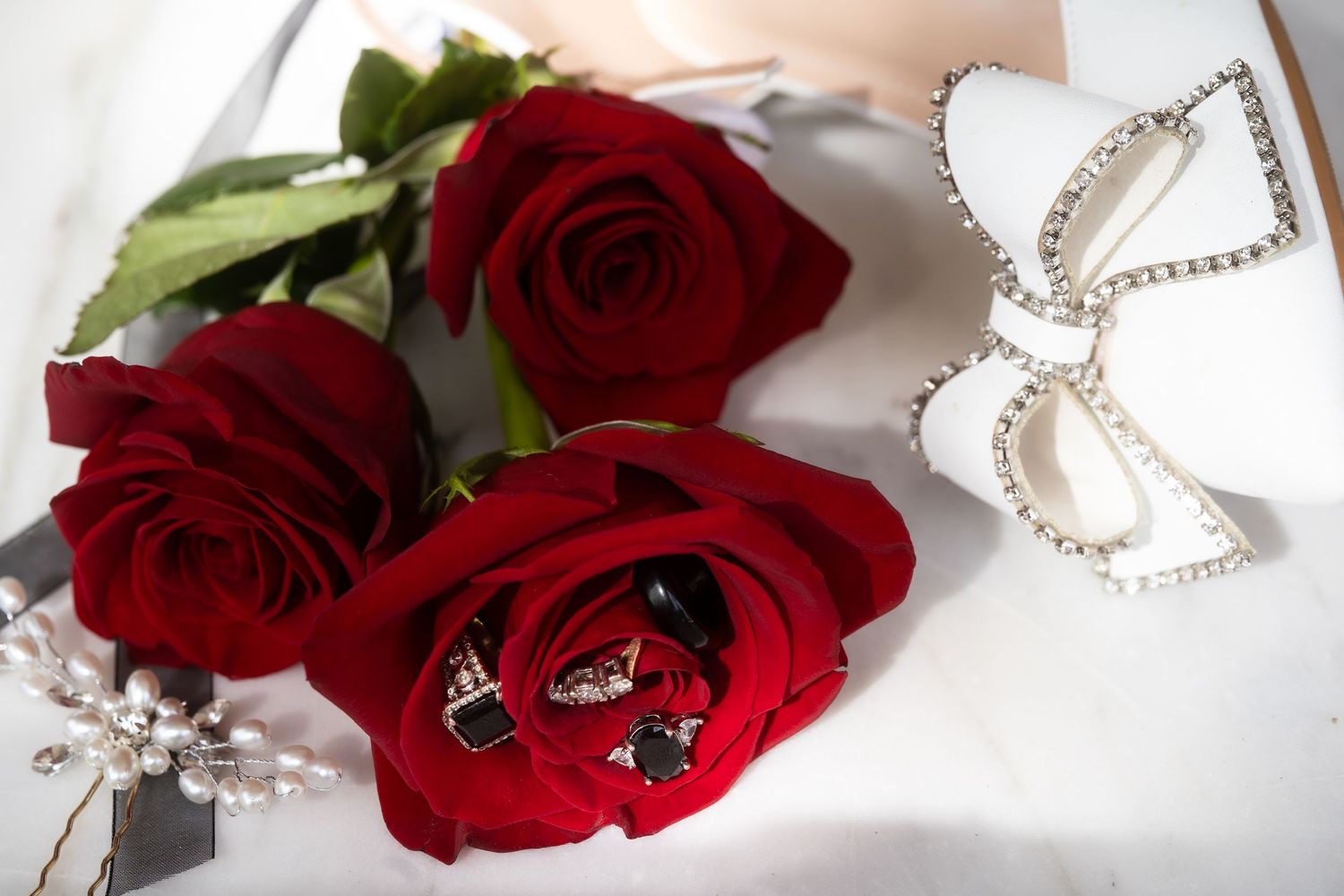 Red roses and pearl necklaces arranged on a white surface for a romantic wedding detail shot.